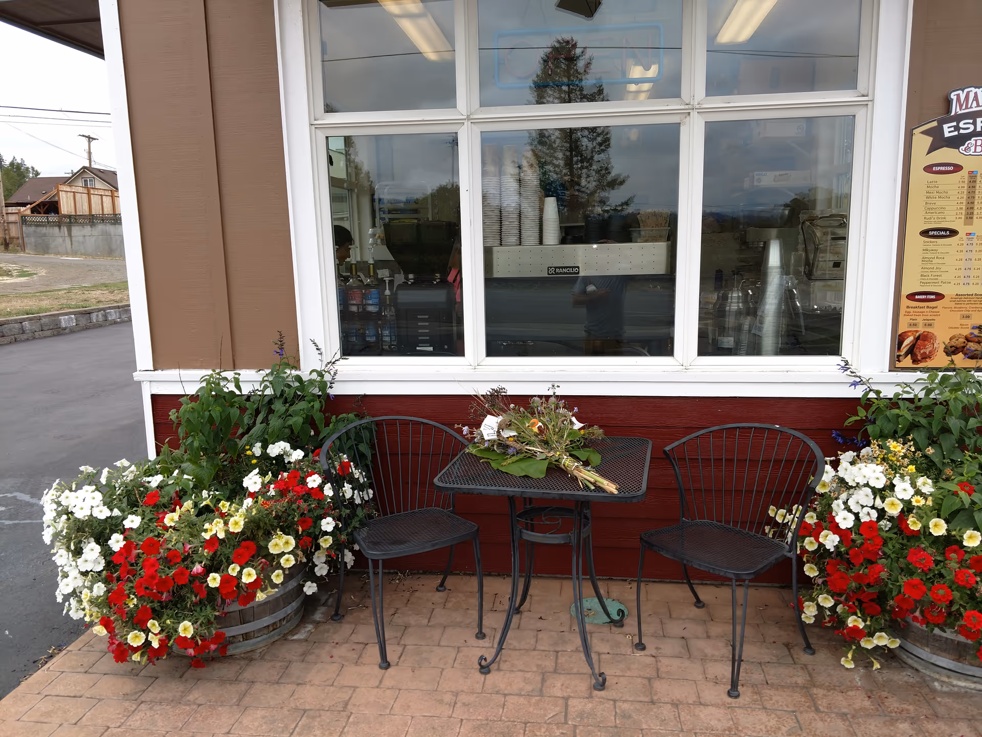 Outdoor seating with a metal table and chairs beside a flower-filled storefront window.