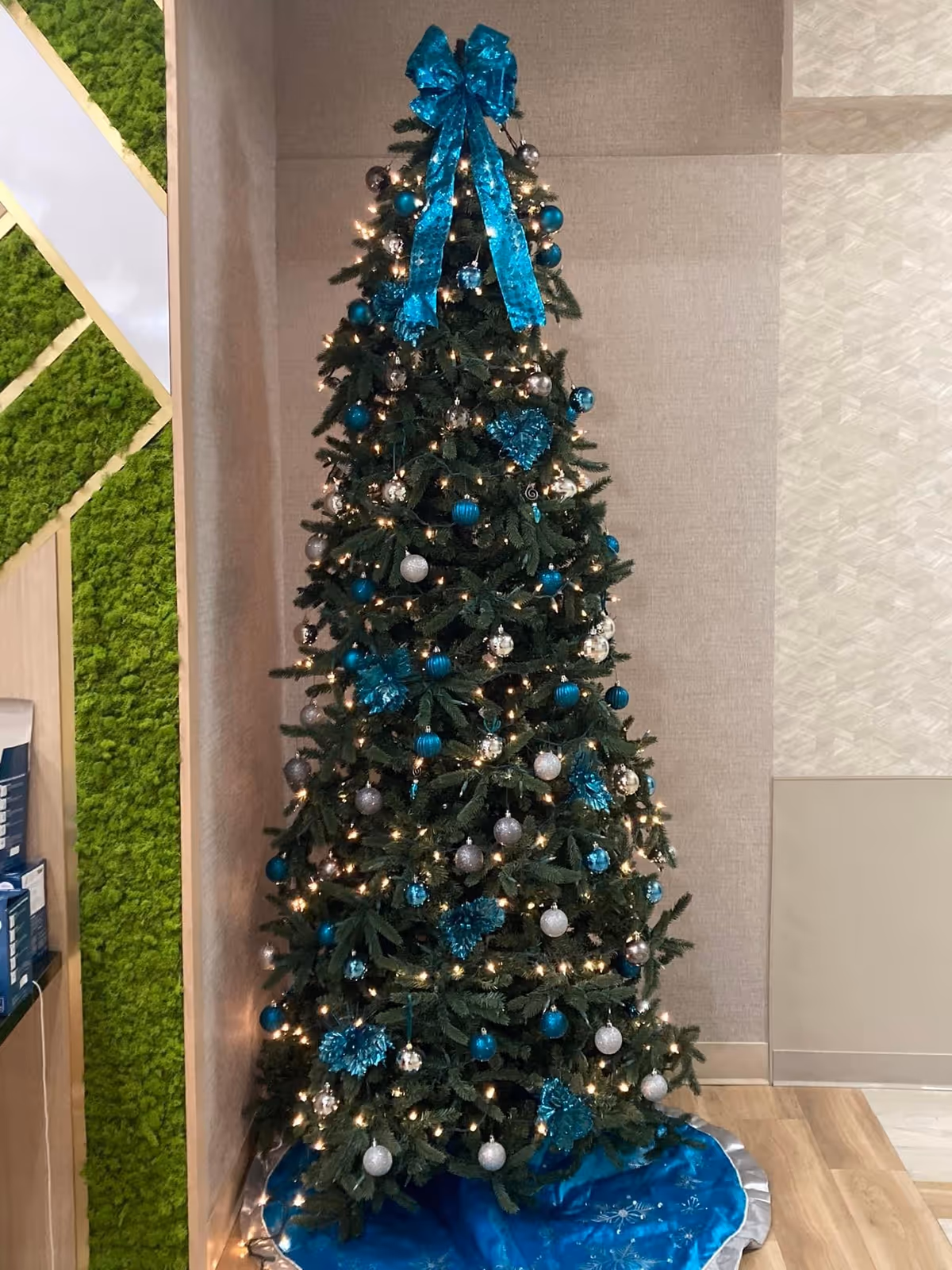 Christmas tree decorated with teal and silver ornaments and white lights standing in an interior corner.