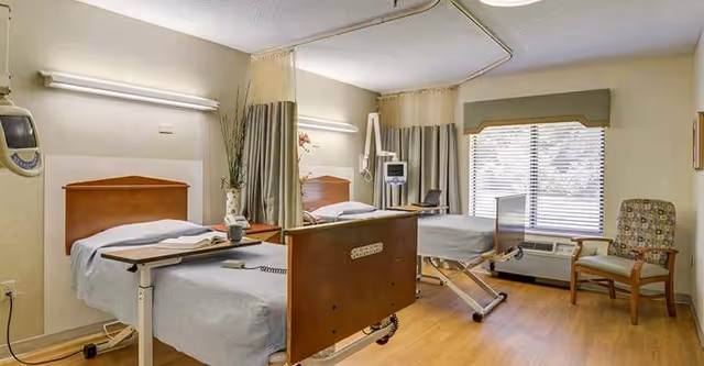 Two hospital beds in a shared patient room with curtains, medical equipment, and a window.
