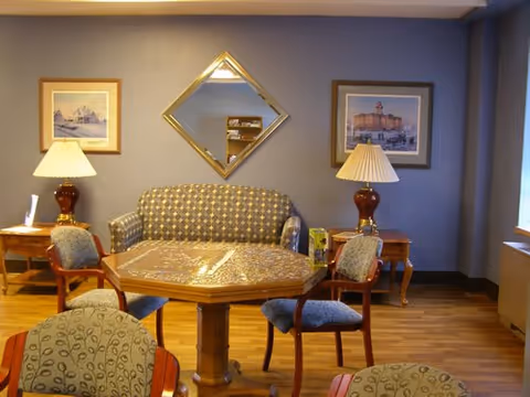 A cozy dining room with a round wooden table, chairs, lamps, and wall art.