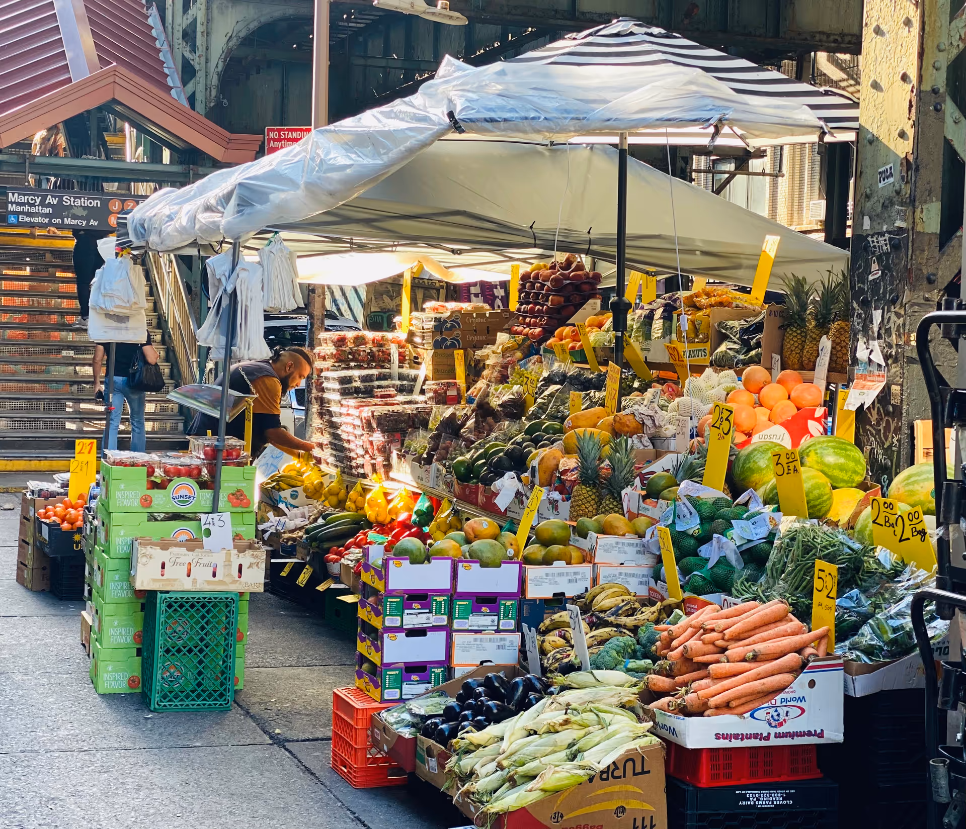 Outdoor street market stall under a canopy with colorful fruits and vegetables.