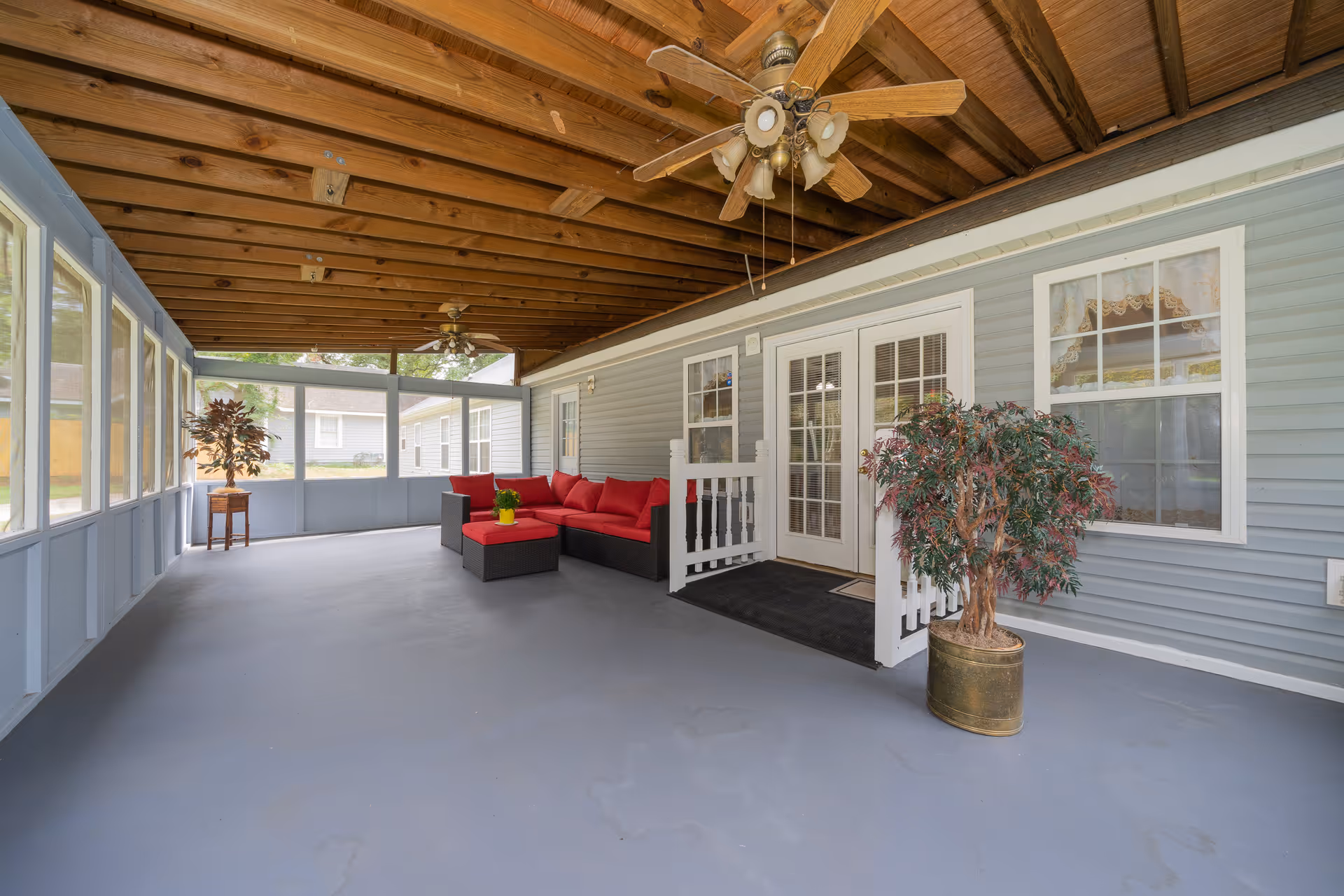 Covered screened porch with red-cushioned seating and ceiling fans.