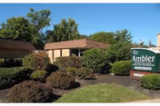 Single-story beige building with manicured shrubs and an Ambler Extended Care Center sign.