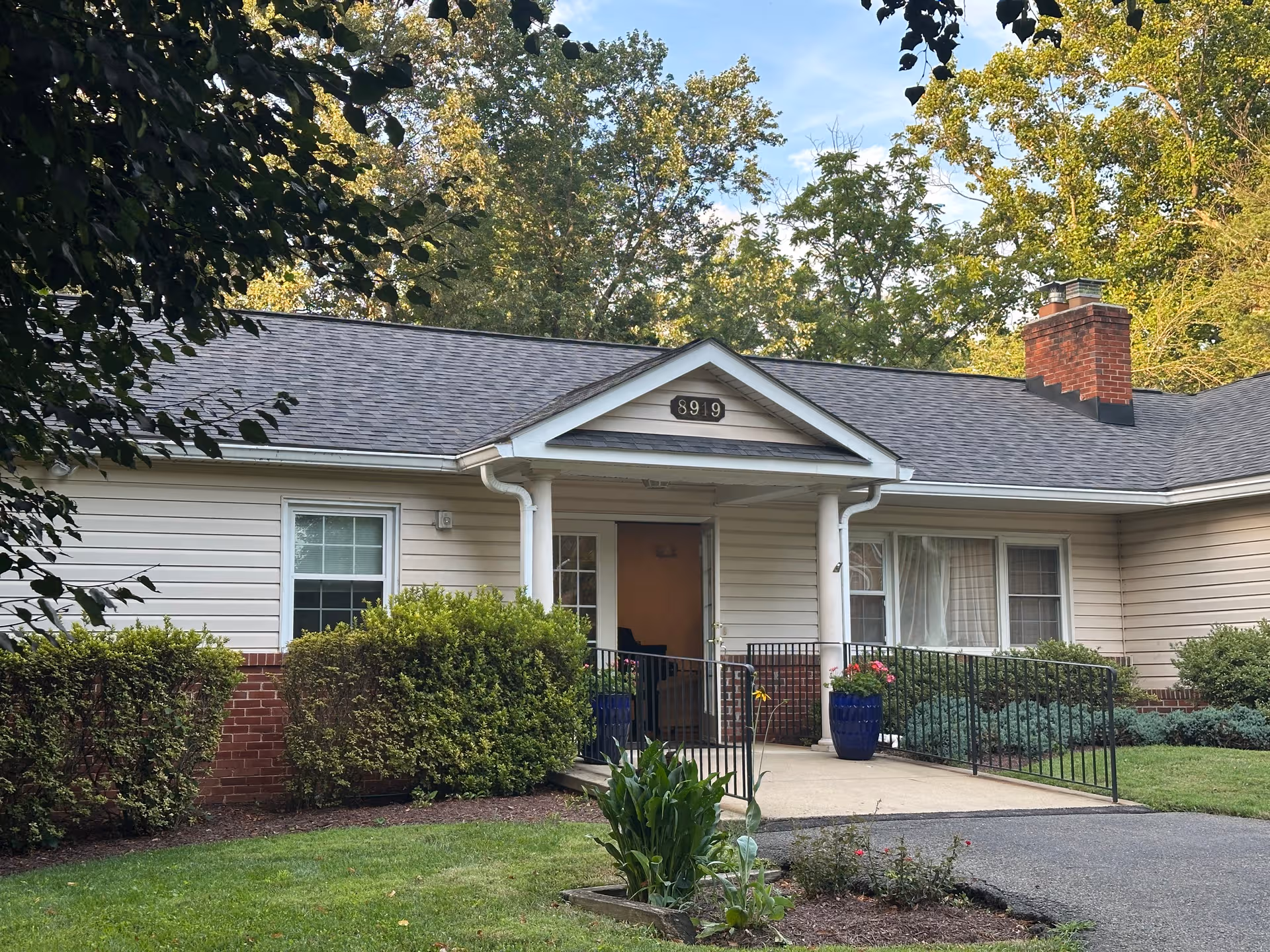 Single-story beige building front with a covered entrance, railing, and well-kept landscaping.