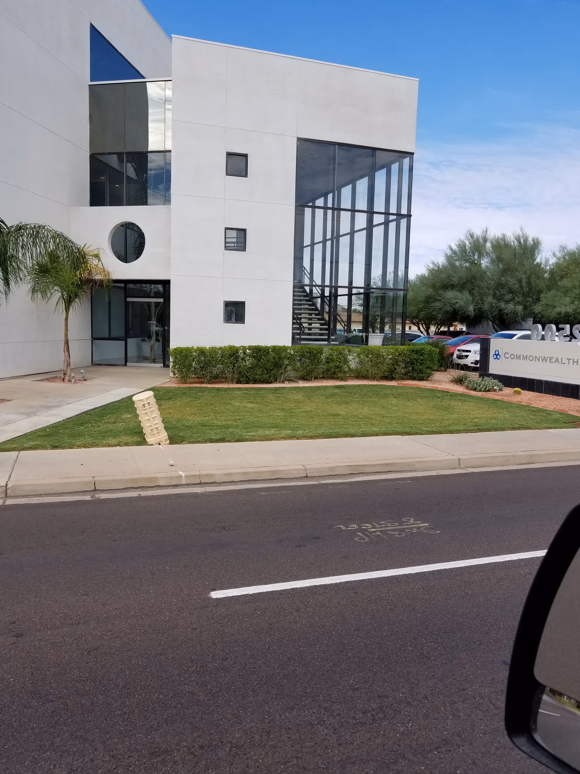 Modern white building with large glass facade and manicured lawn beside the street.