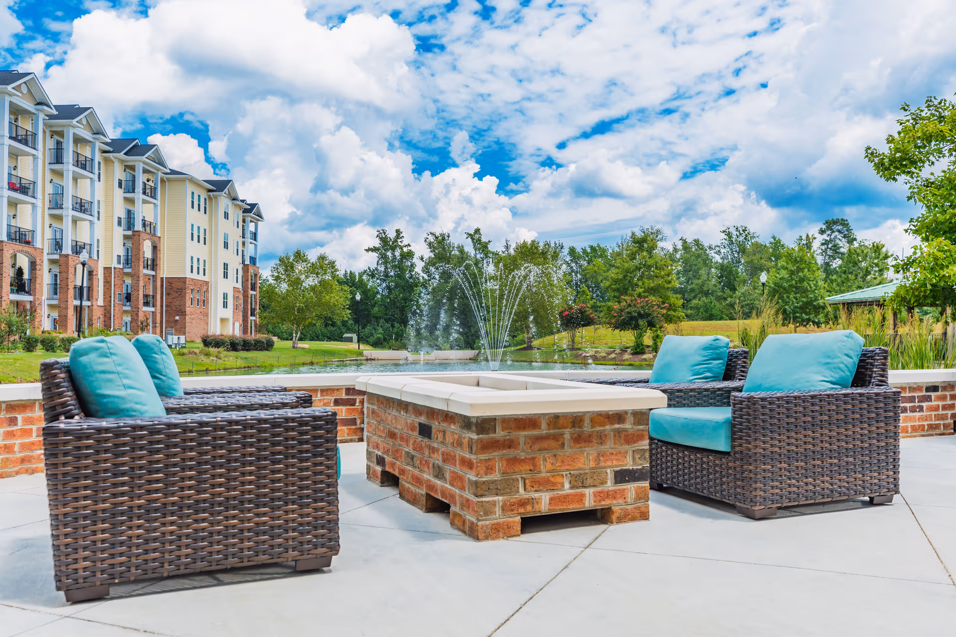 Outdoor seating area with wicker chairs around a brick fire pit and fountain.
