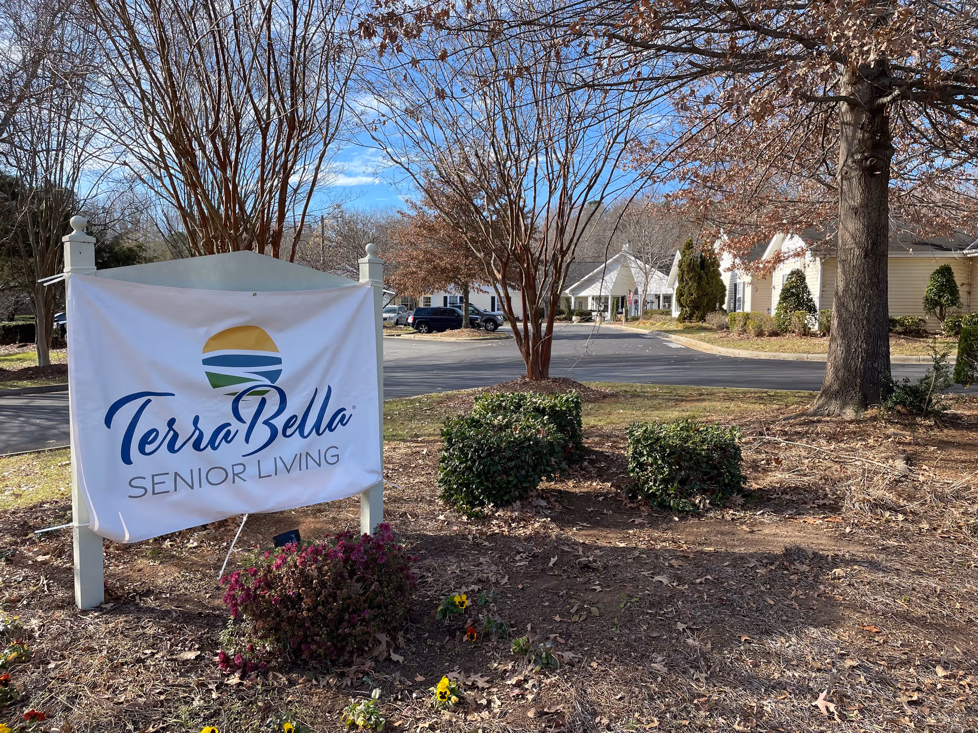 TerraBella Senior Living sign in a landscaped front yard with trees.