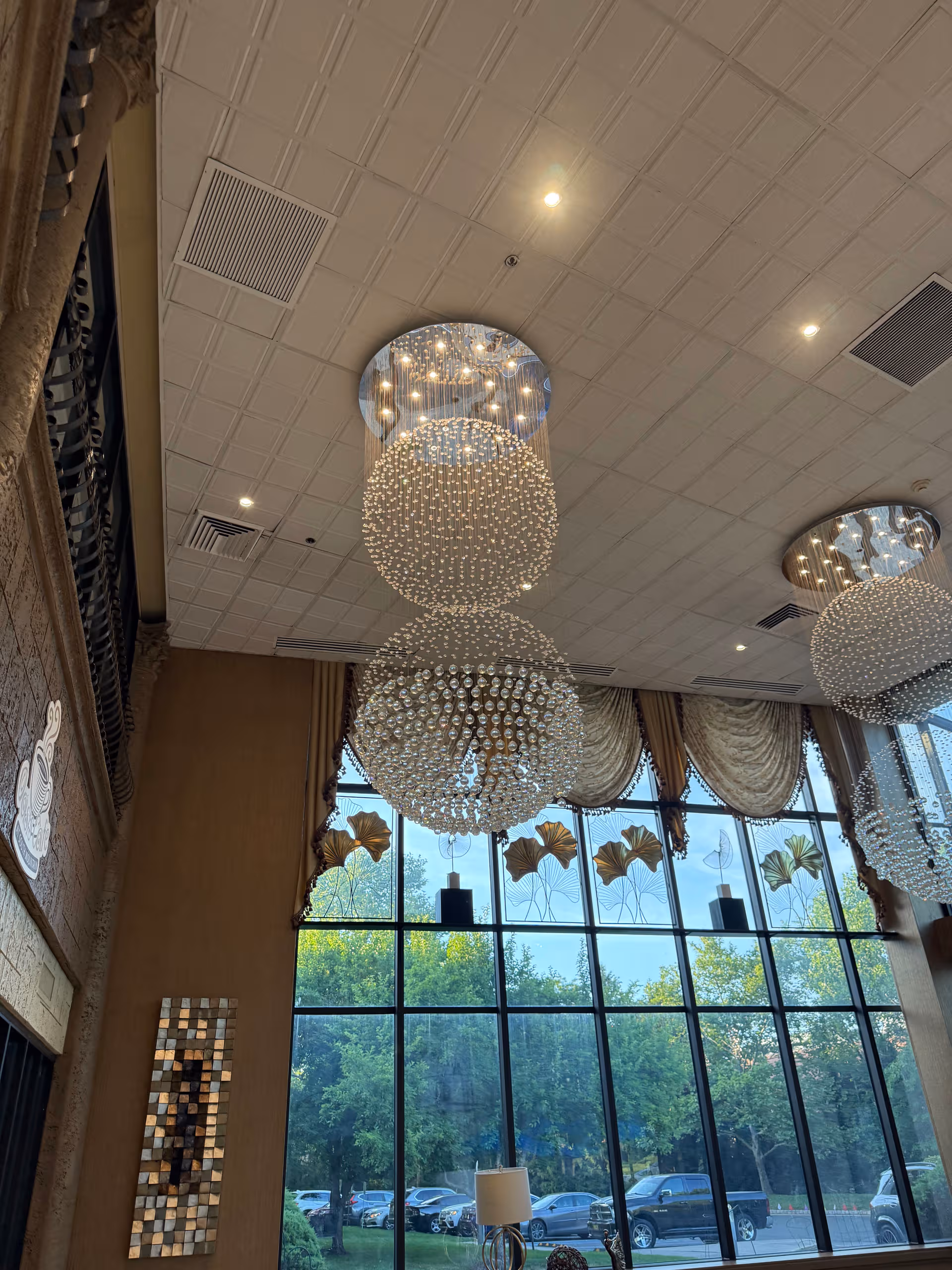 Tall lobby area with large crystal chandeliers, floor-to-ceiling windows, and draped curtains.
