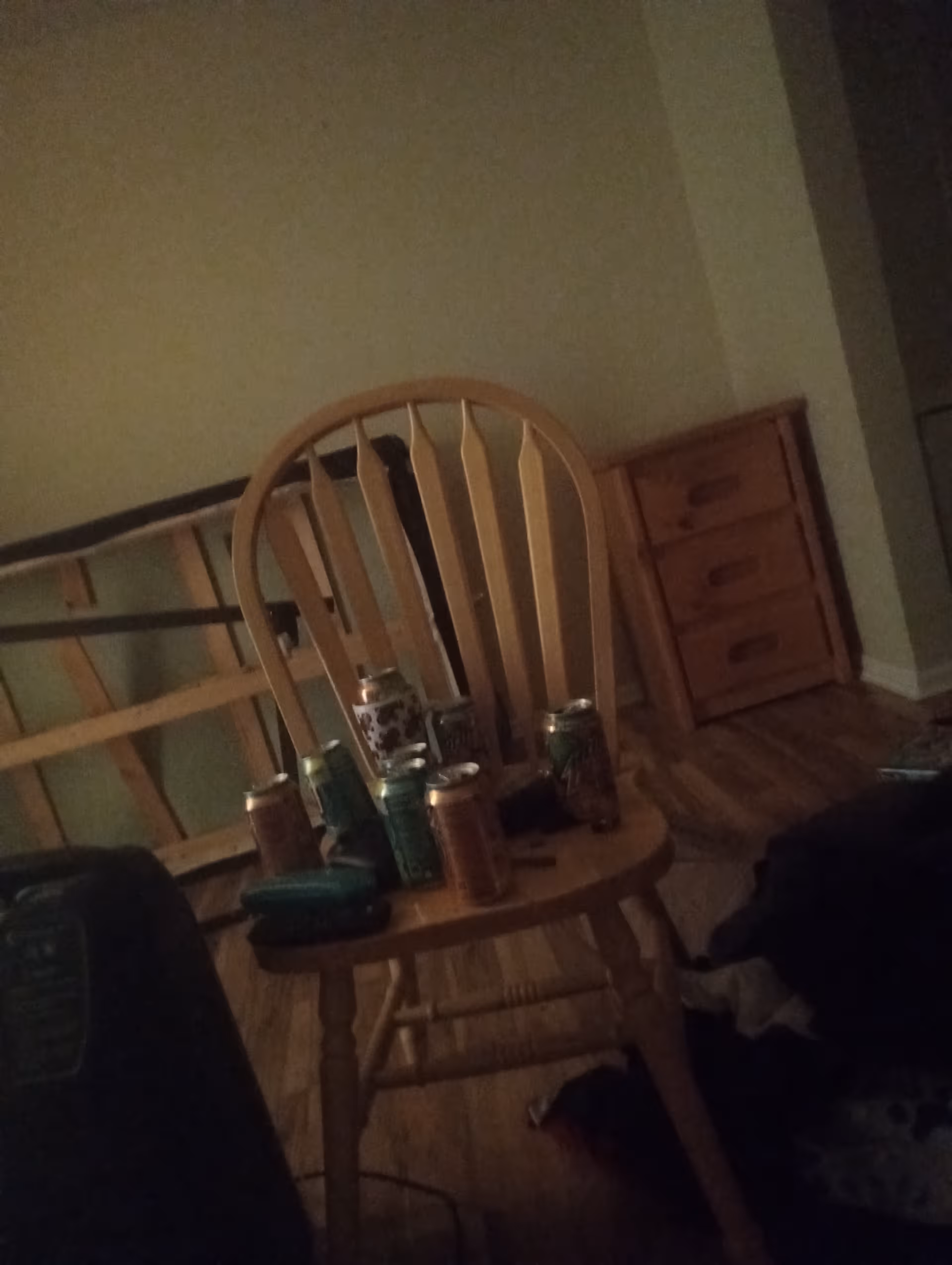 Dimly lit bedroom interior with a wooden chair and cluttered table holding beverage cans.