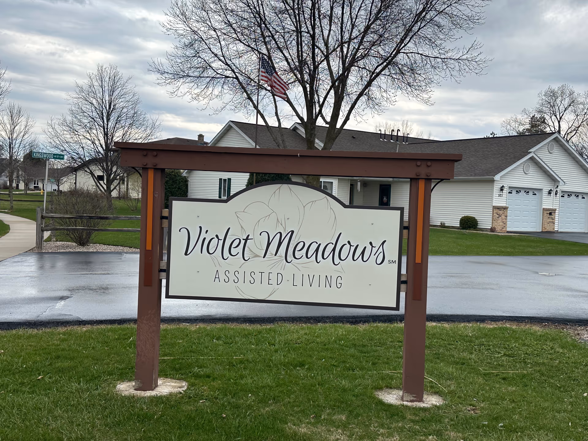 Outdoor view of a senior living facility sign labeled Violet Meadows with a residential building behind.