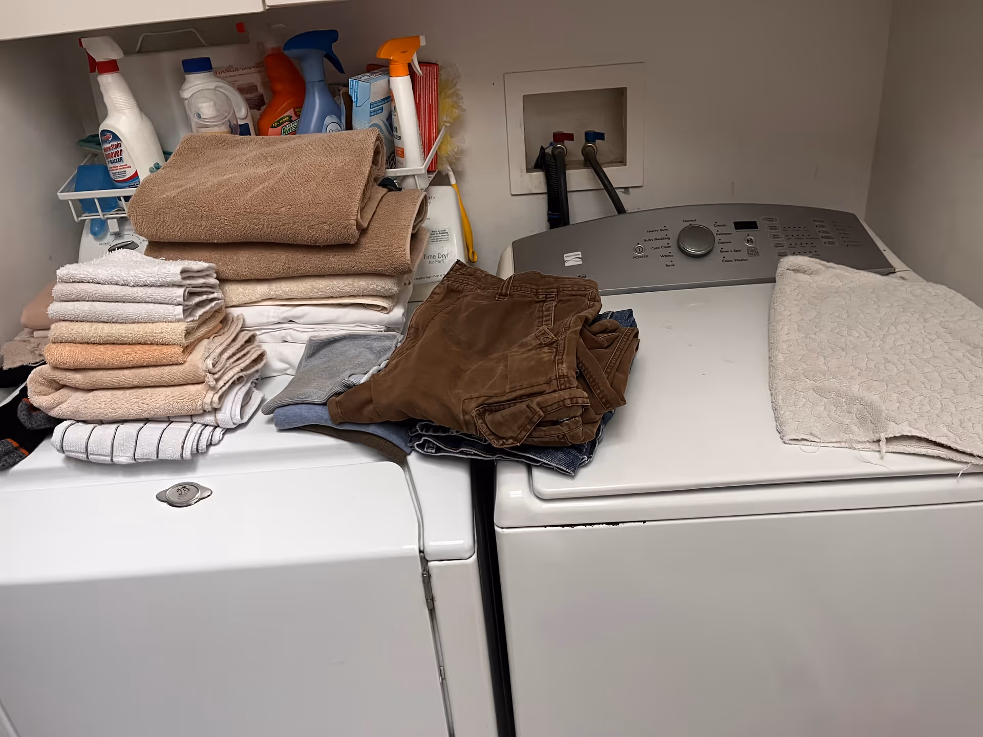 Laundry area with stacked towels, clothes, cleaning supplies, and a washer-dryer unit.