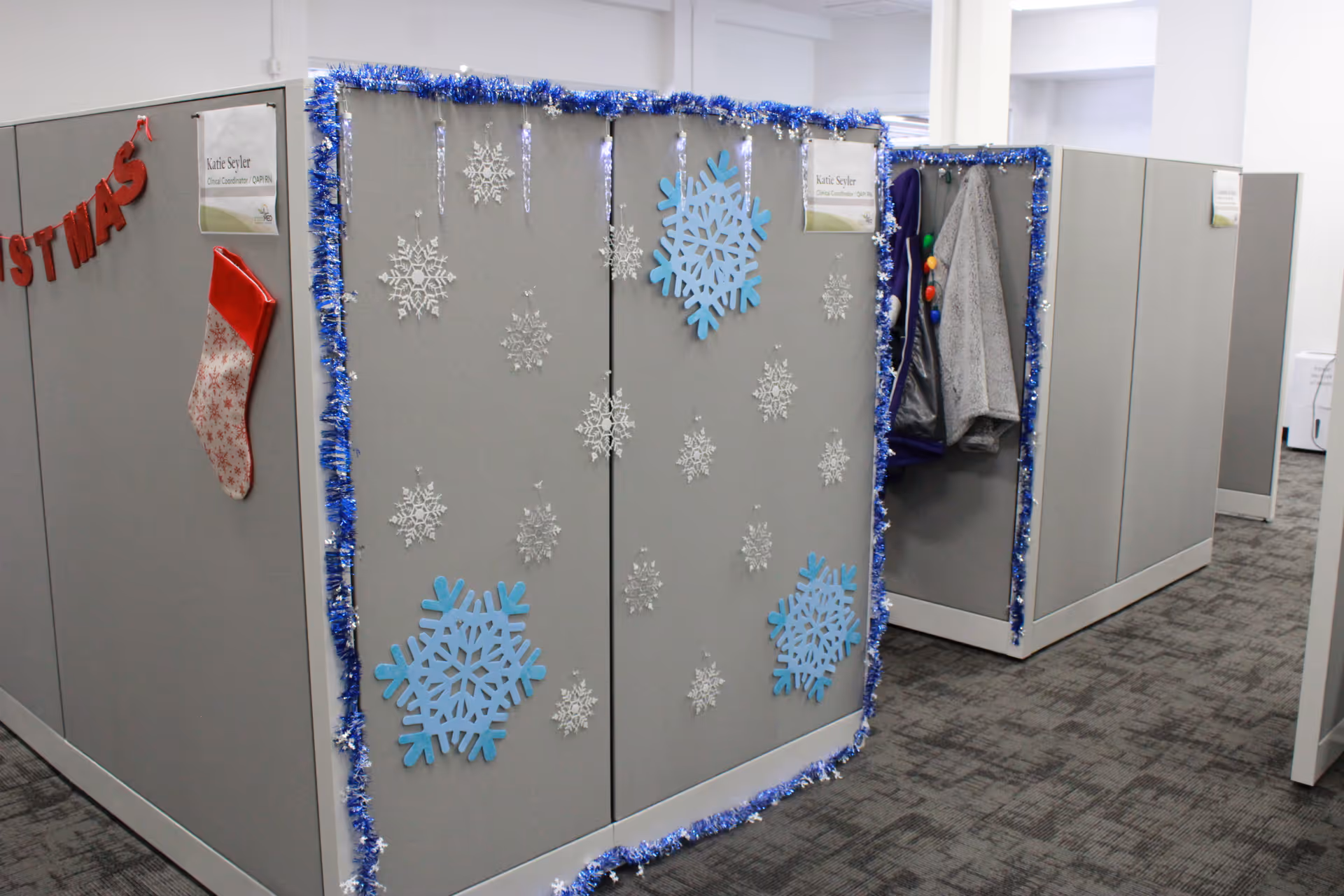 Decorated office cubicles in a senior living facility hallway with snowflake garlands.