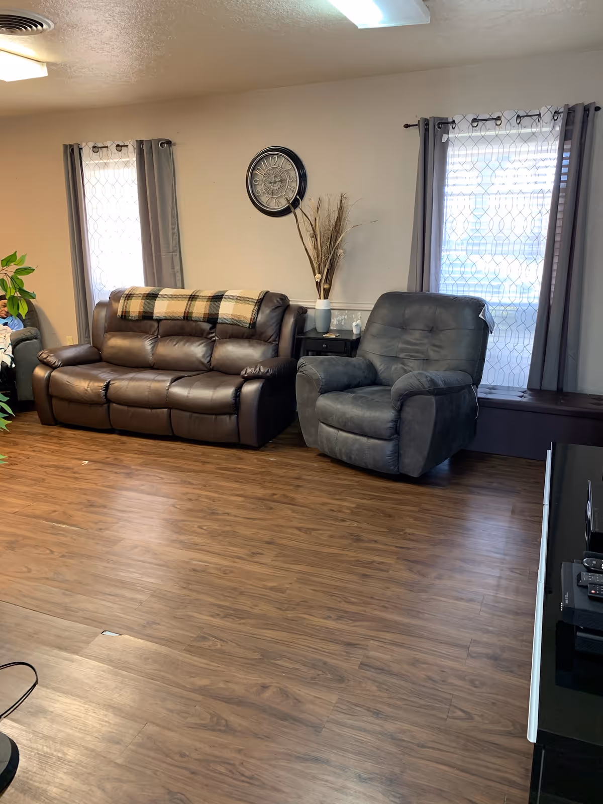 Cozy living room with brown leather sofa, recliner, curtains, wall clock, and decor.