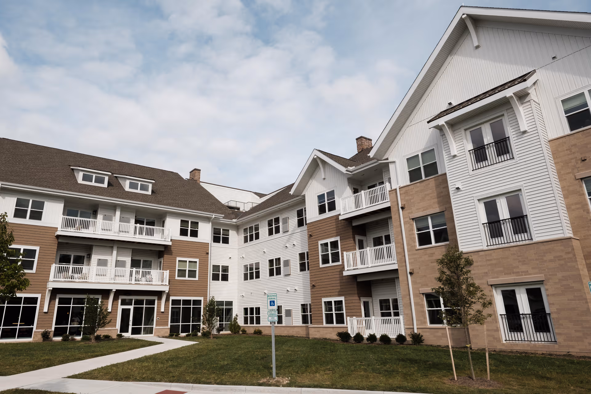 Front exterior of a multi-story senior living building with balconies, many windows, and a small lawn.