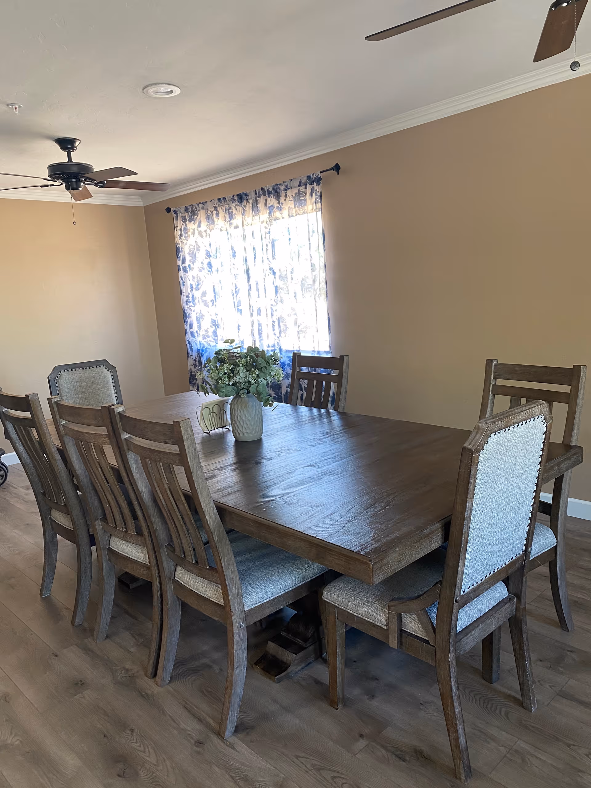 A large wooden dining table with chairs in a sunlit dining room.