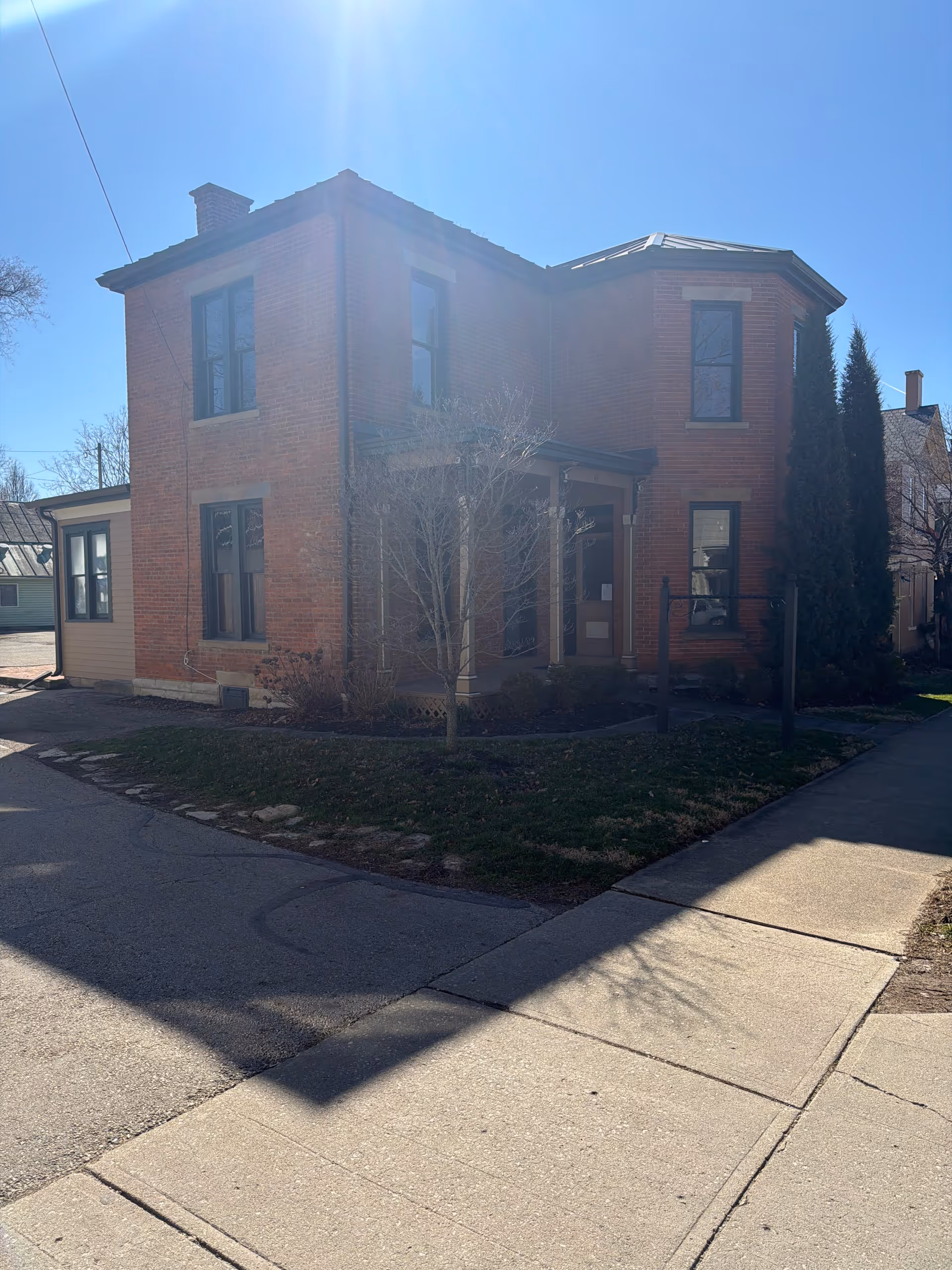Brick two-story building with front entrance and sidewalk, framed by bare trees.