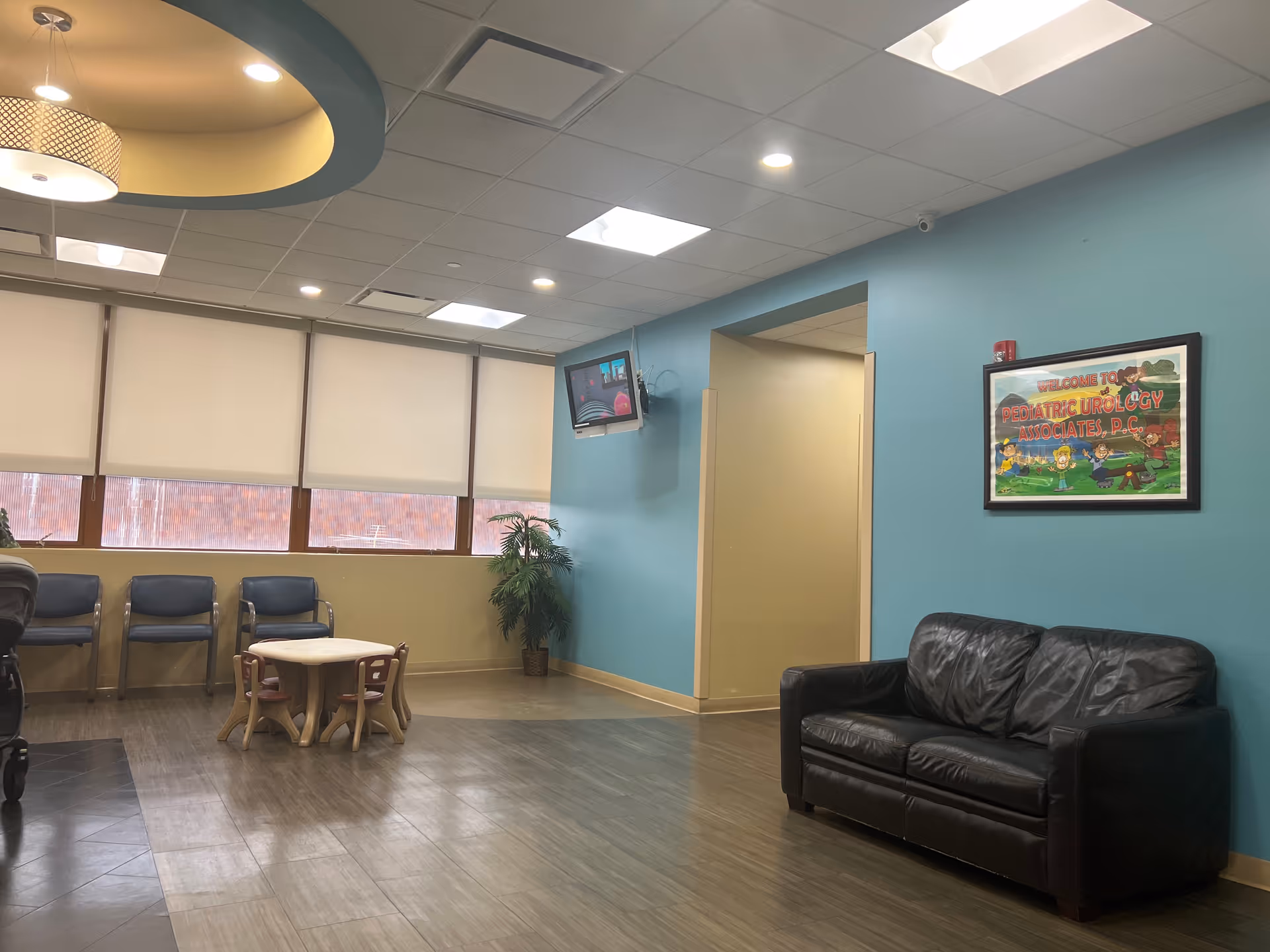 A modern waiting area with teal walls, a black leather sofa, and kid-sized table and chairs.