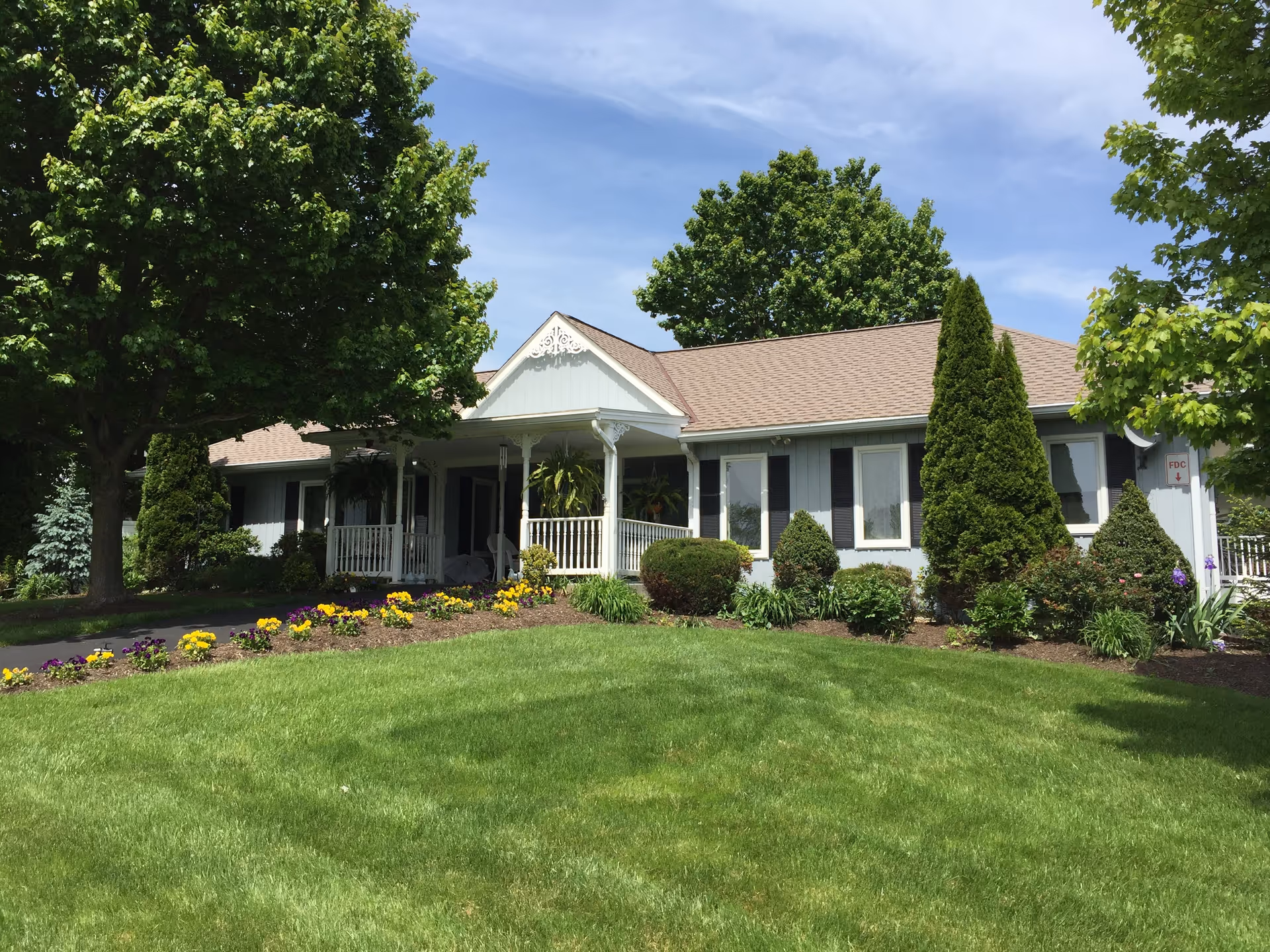 Front exterior of a single-story senior living home with a manicured lawn and landscaping.