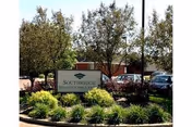 Exterior view of a senior care facility sign surrounded by greenery and parked cars.