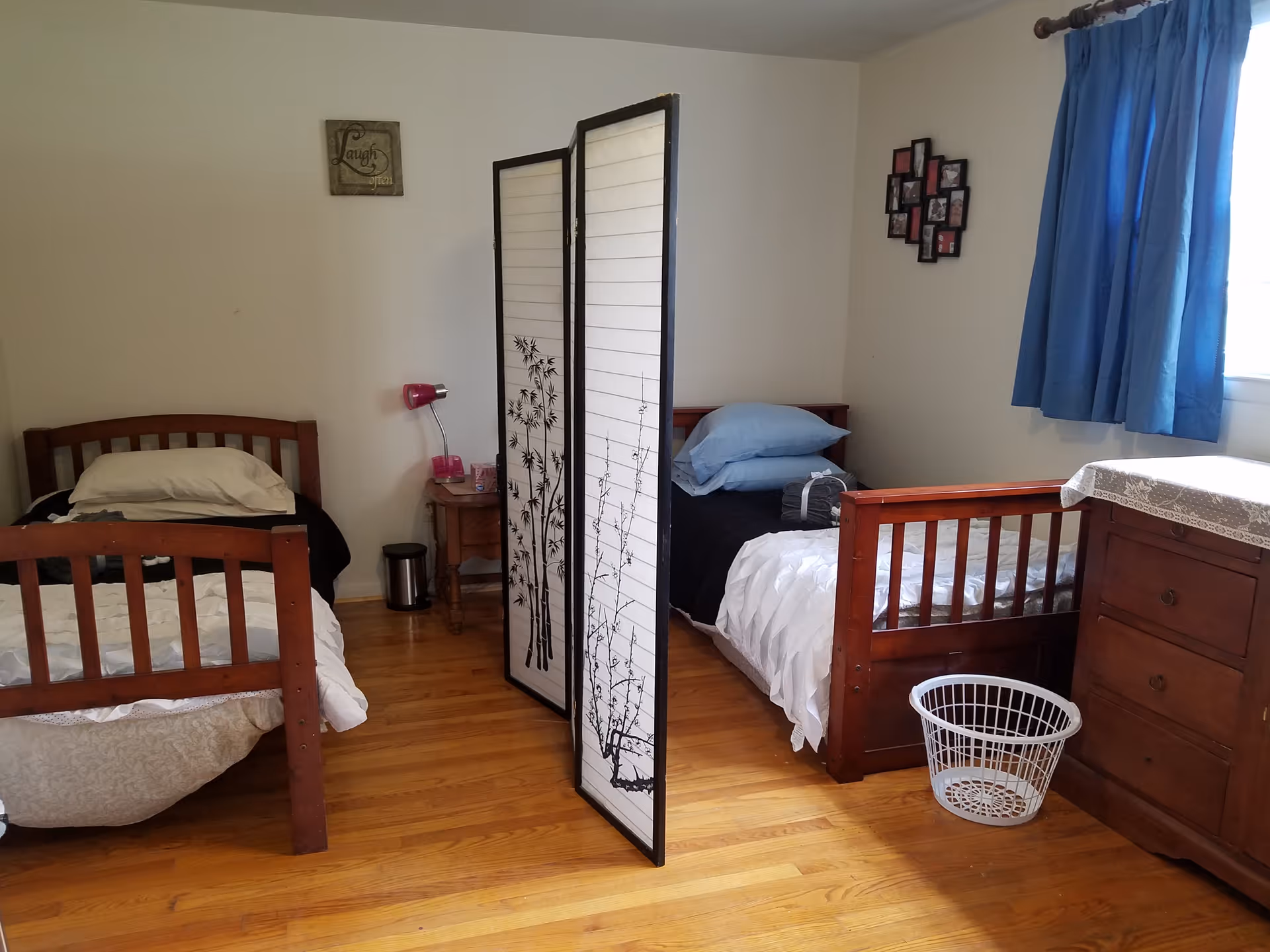 A shared bedroom with two wooden beds separated by a folding screen and blue curtains.