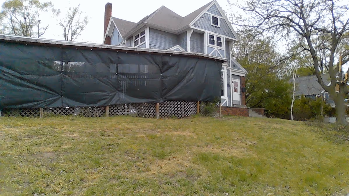 Exterior view of Gibbs Place showing a light-blue house with a large tarped side structure.