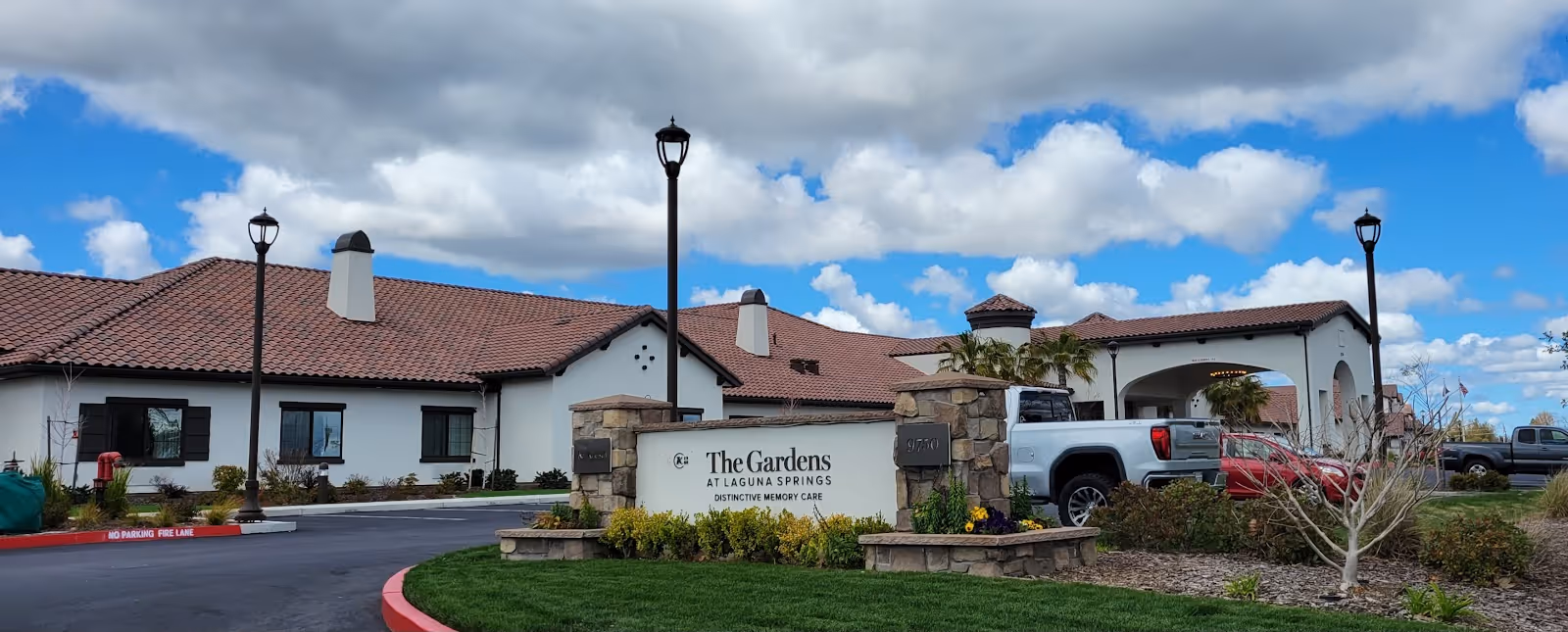Exterior view of Gardens at Laguna Springs building with sign, landscaping, and parked cars.