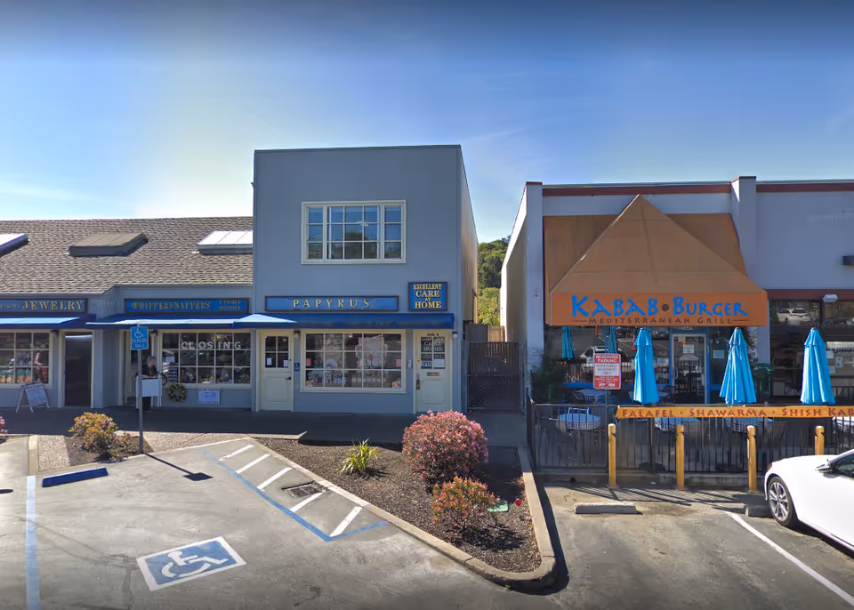 Row of storefronts including Excellent Care At Home and Kabab Burger with outdoor seating.
