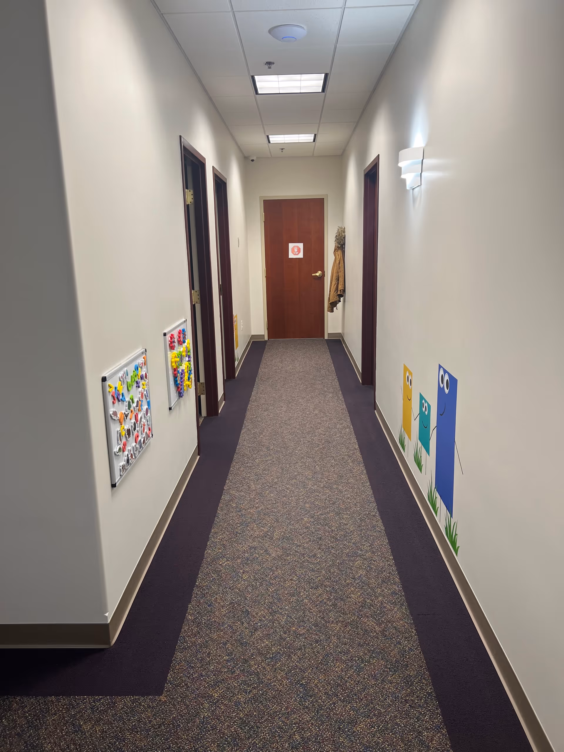 A well-lit hallway in a senior living facility with multiple doors and colorful wall art.