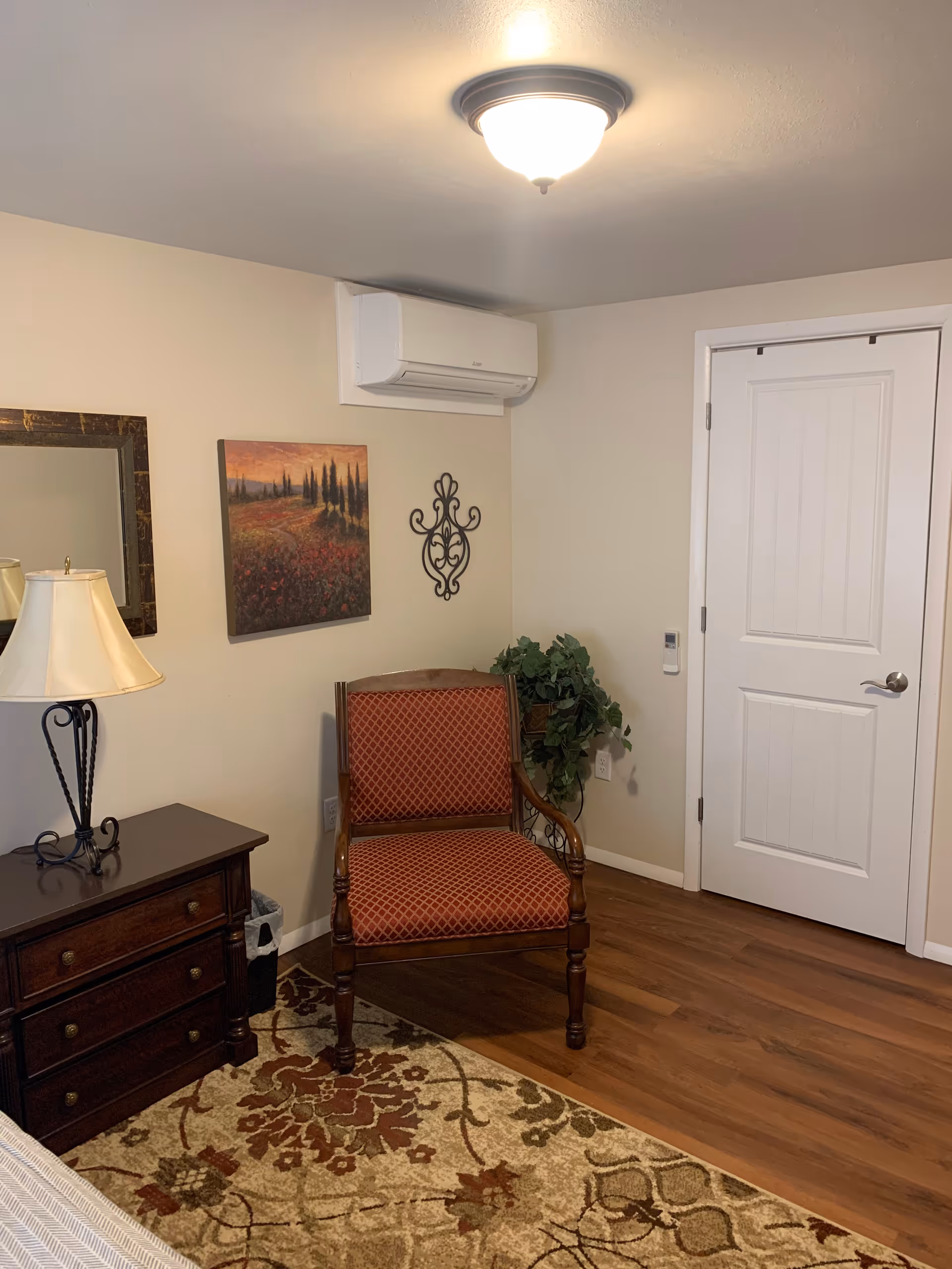 Small living room corner with chair, dresser, lamp, plant, and door.