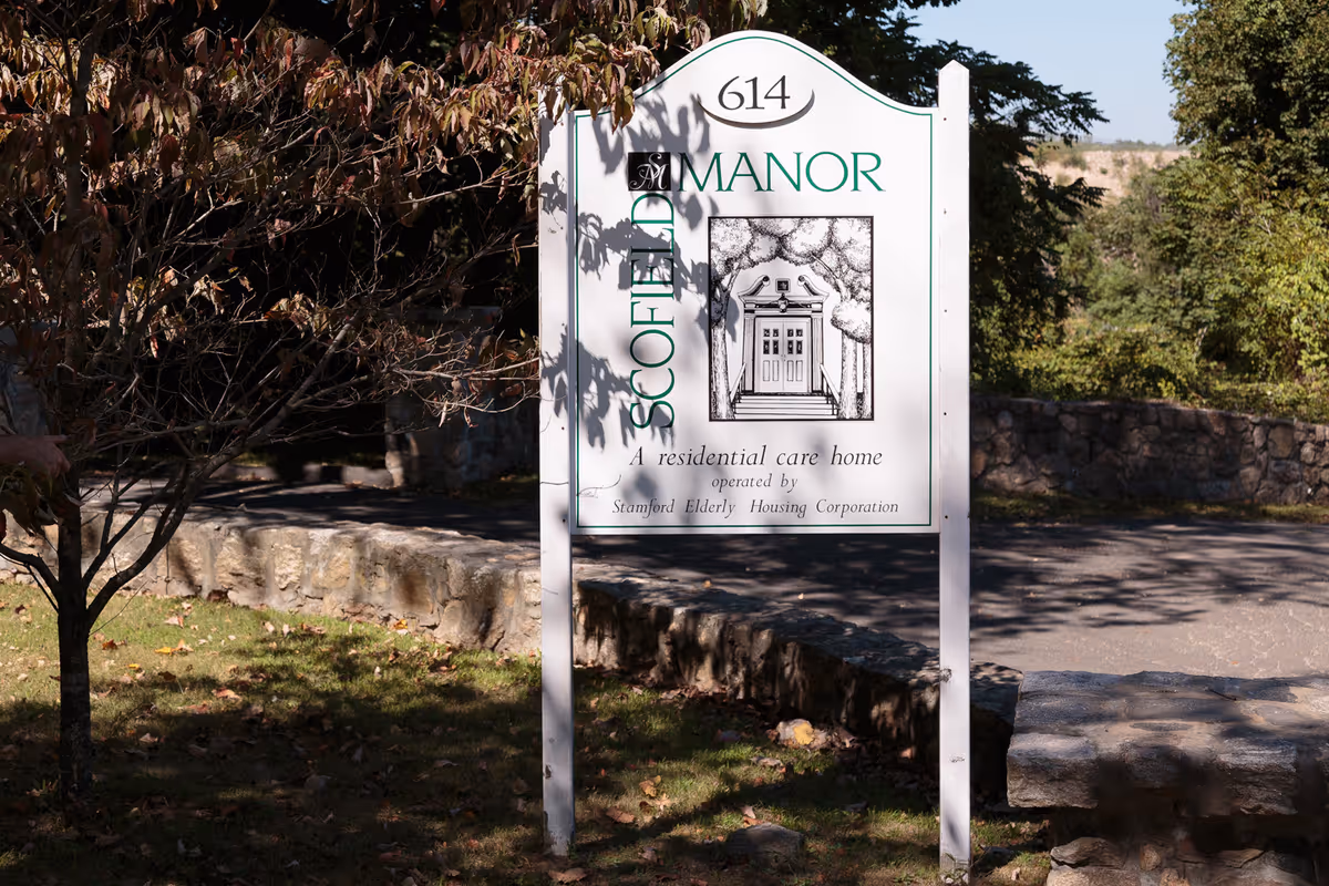White freestanding sign reading 'Scofield Manor' with the number 614 marking a residential care home at an outdoor entrance.