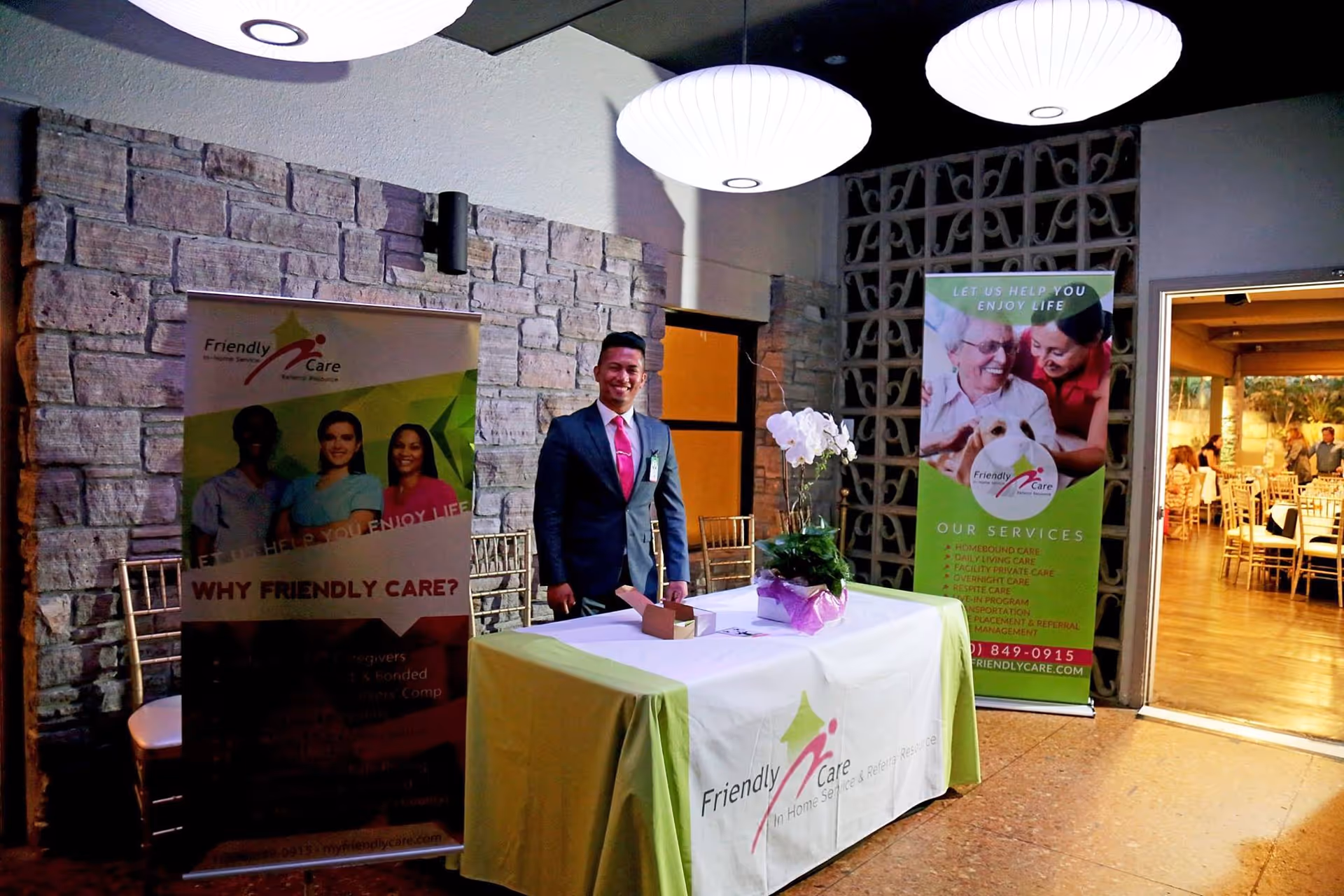 Staff in suit at bannered reception desk inside Friendly Care facility lobby.