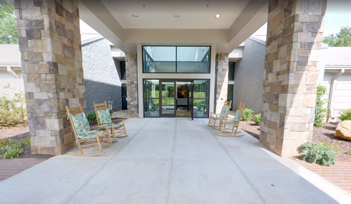 Covered entrance with stone pillars, wooden rocking chairs, and glass double doors into the facility.