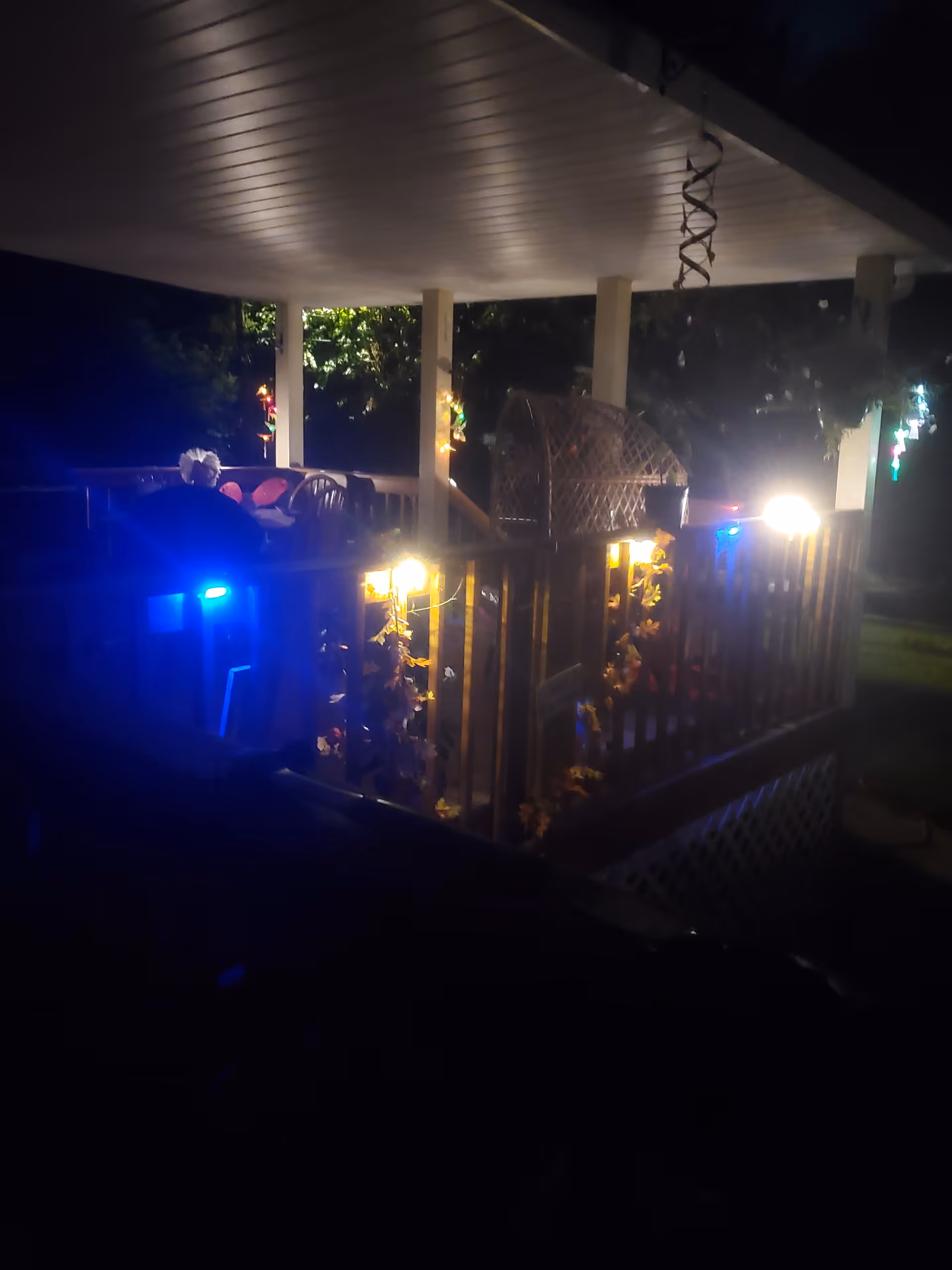 Night exterior porch of a decorated senior home with railing, lights, and a resident seated.