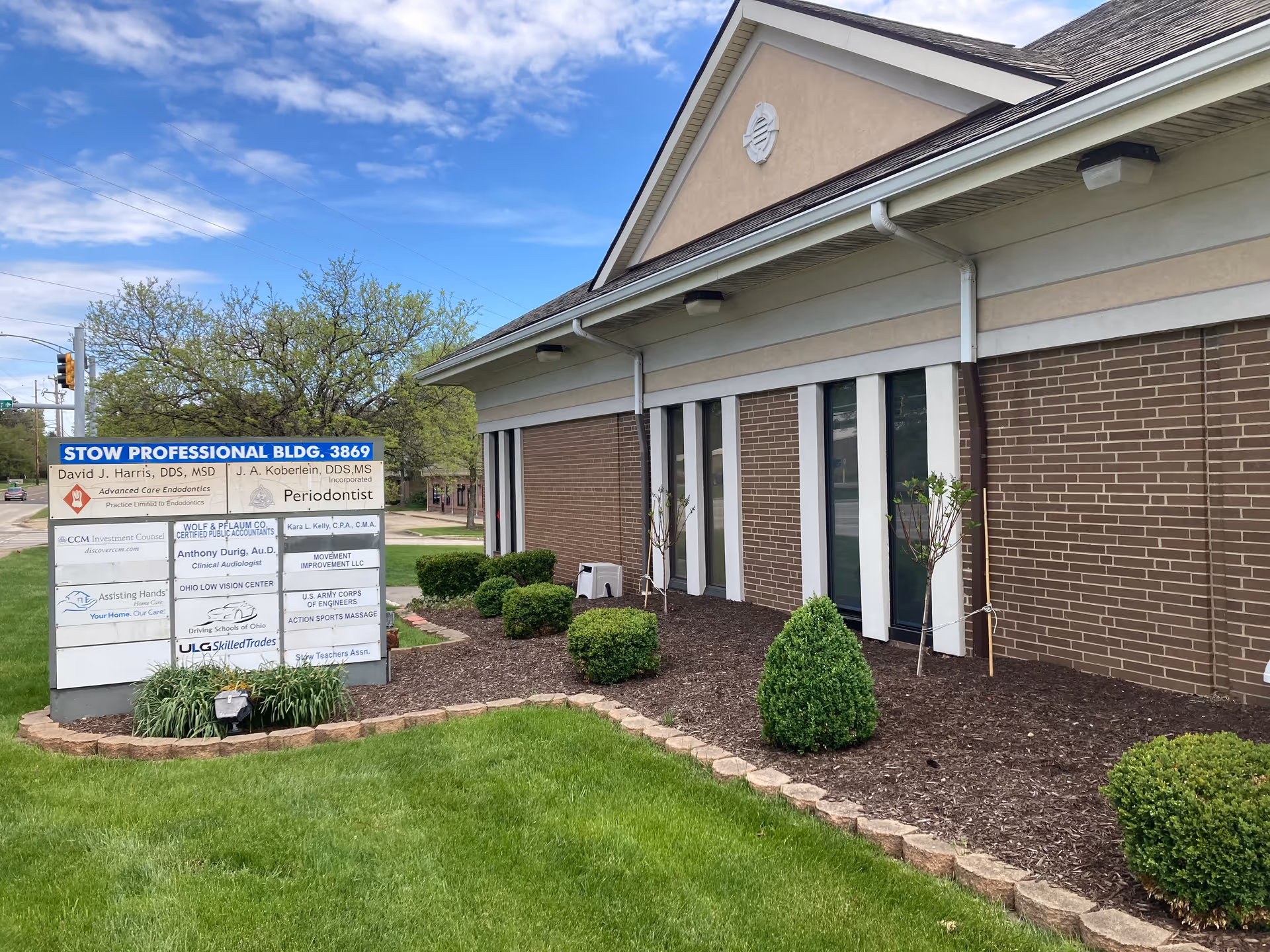 Exterior view of a brick building with a blue multi-tenant signboard near landscaping.