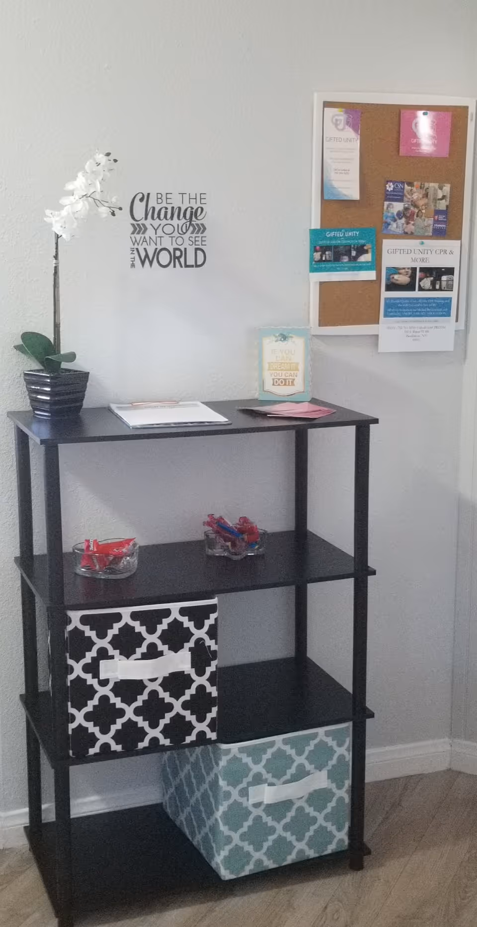 A black shelving unit with baskets and a bulletin board against a gray wall.