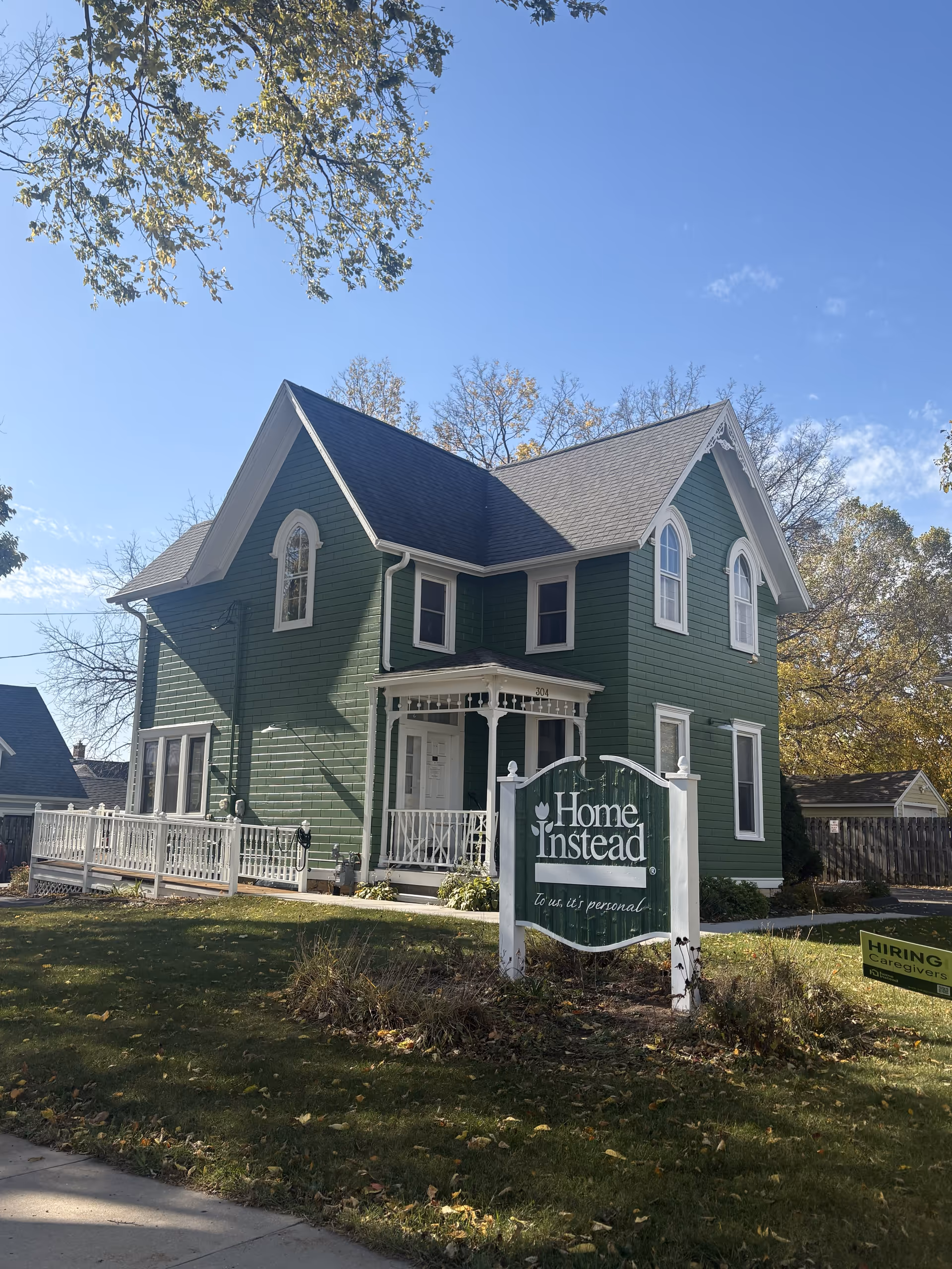 Green two-story building facade with white porch and Home Instead sign in front yard