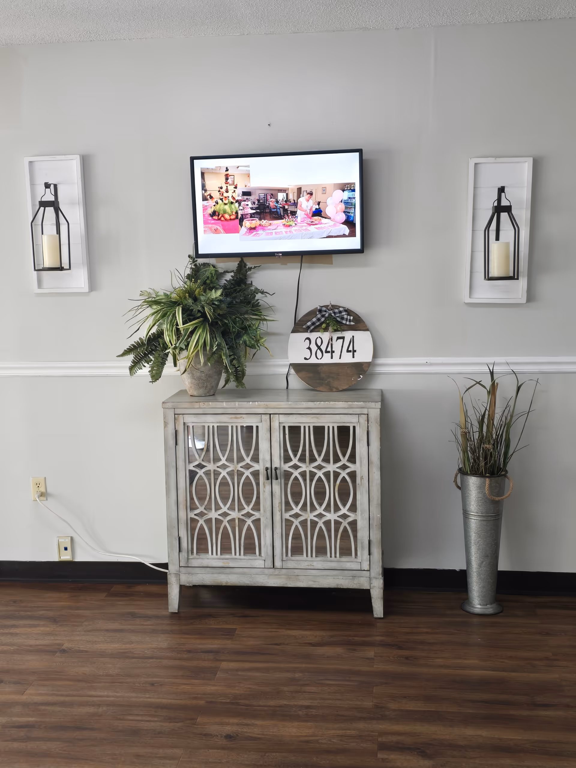 Lobby-style interior with mounted TV, decorative cabinet, lanterns, and plants.
