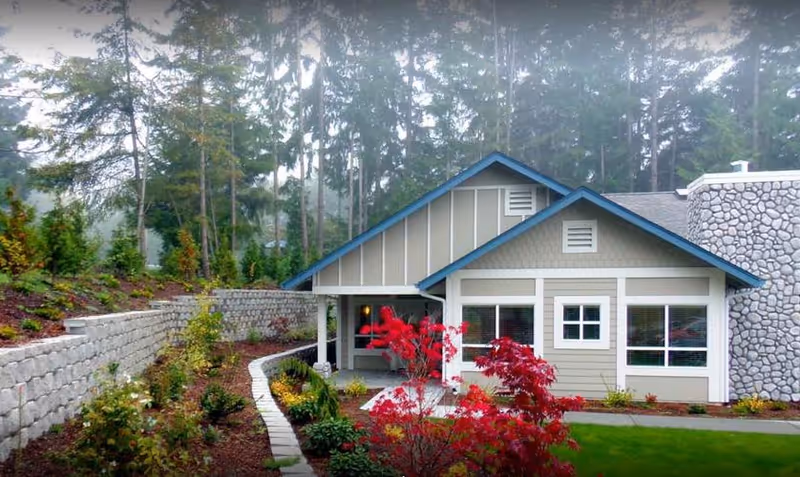 Dramatic view of Northwoods Lodge exterior with stone wall, colorful landscaping, and trees.