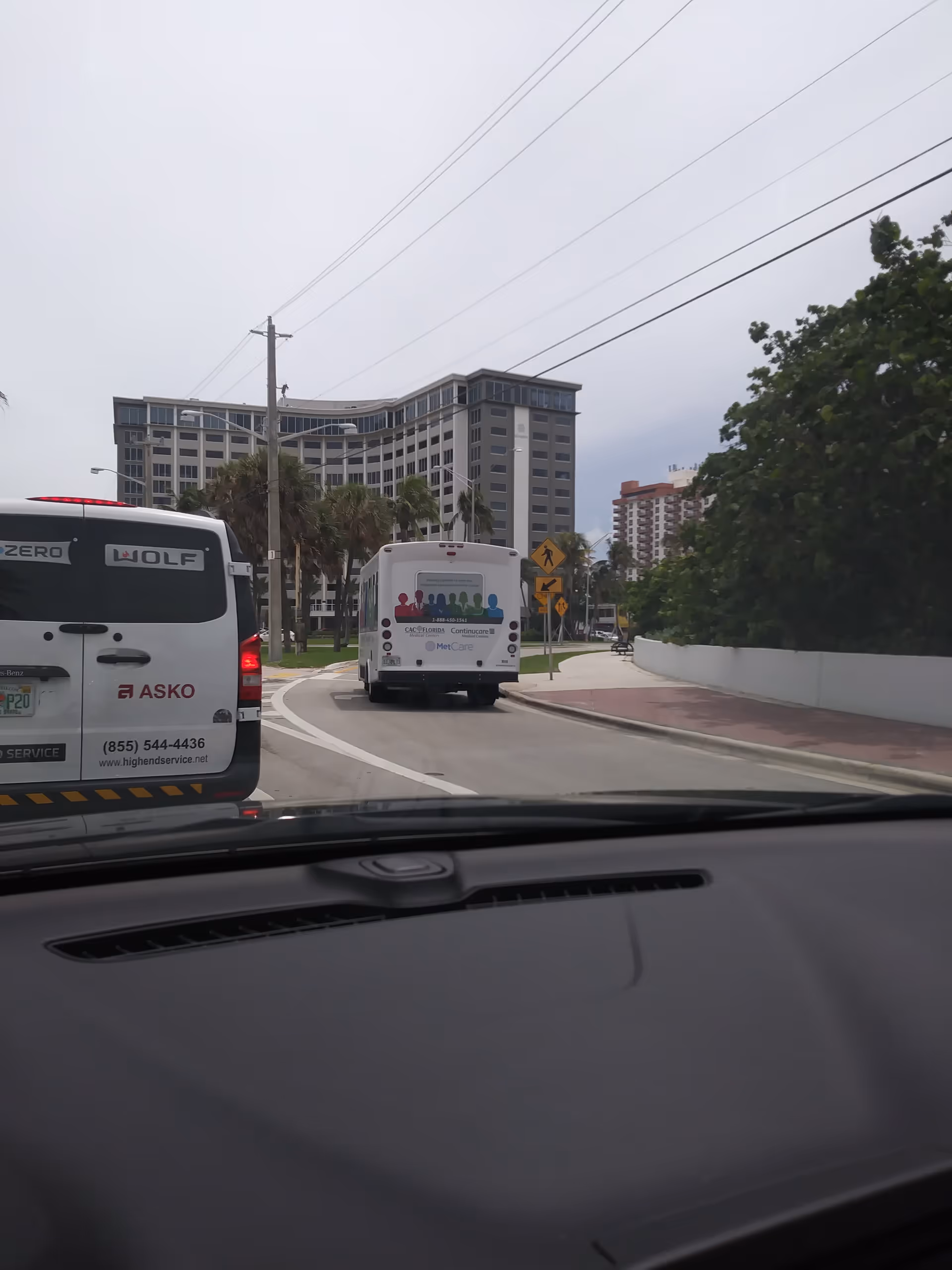 Road scene from a car windshield showing buses and modern buildings nearby.