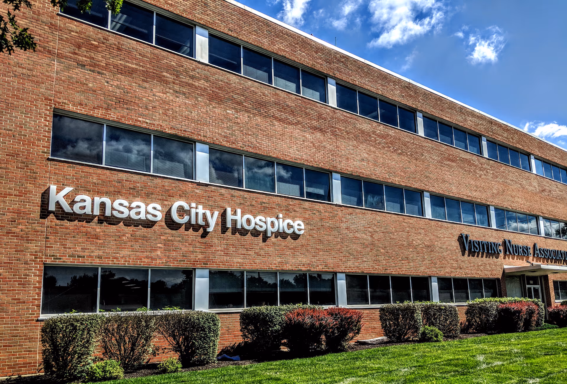 Exterior of Kansas City Hospice building with large windows and trimmed shrubs.
