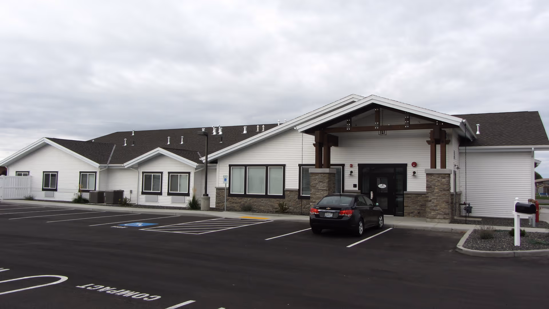 Modern single-story senior living facility exterior with a parking lot and covered entrance.