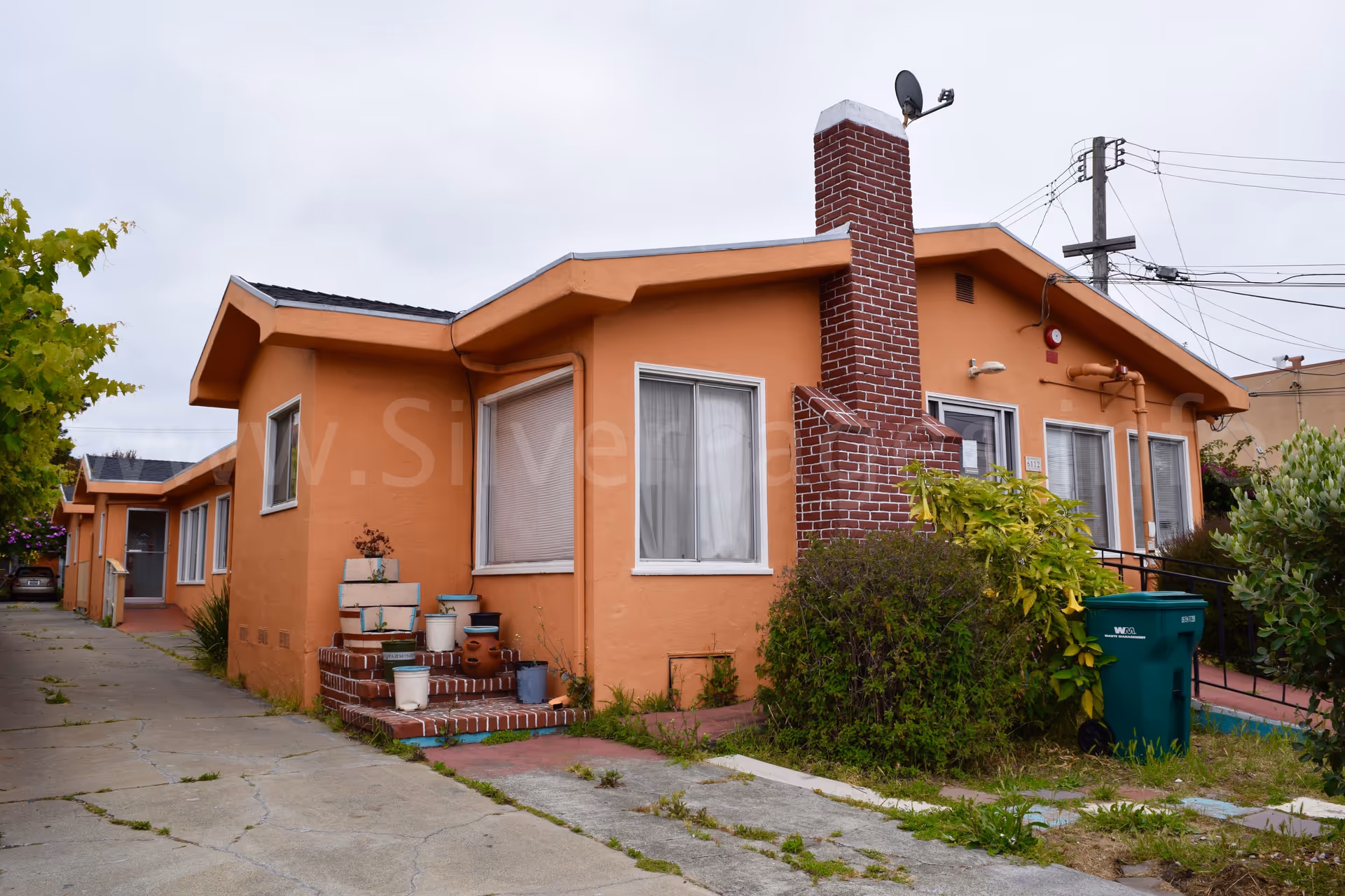 Front exterior of a peach-colored, single-story building with a brick chimney and paved driveway.