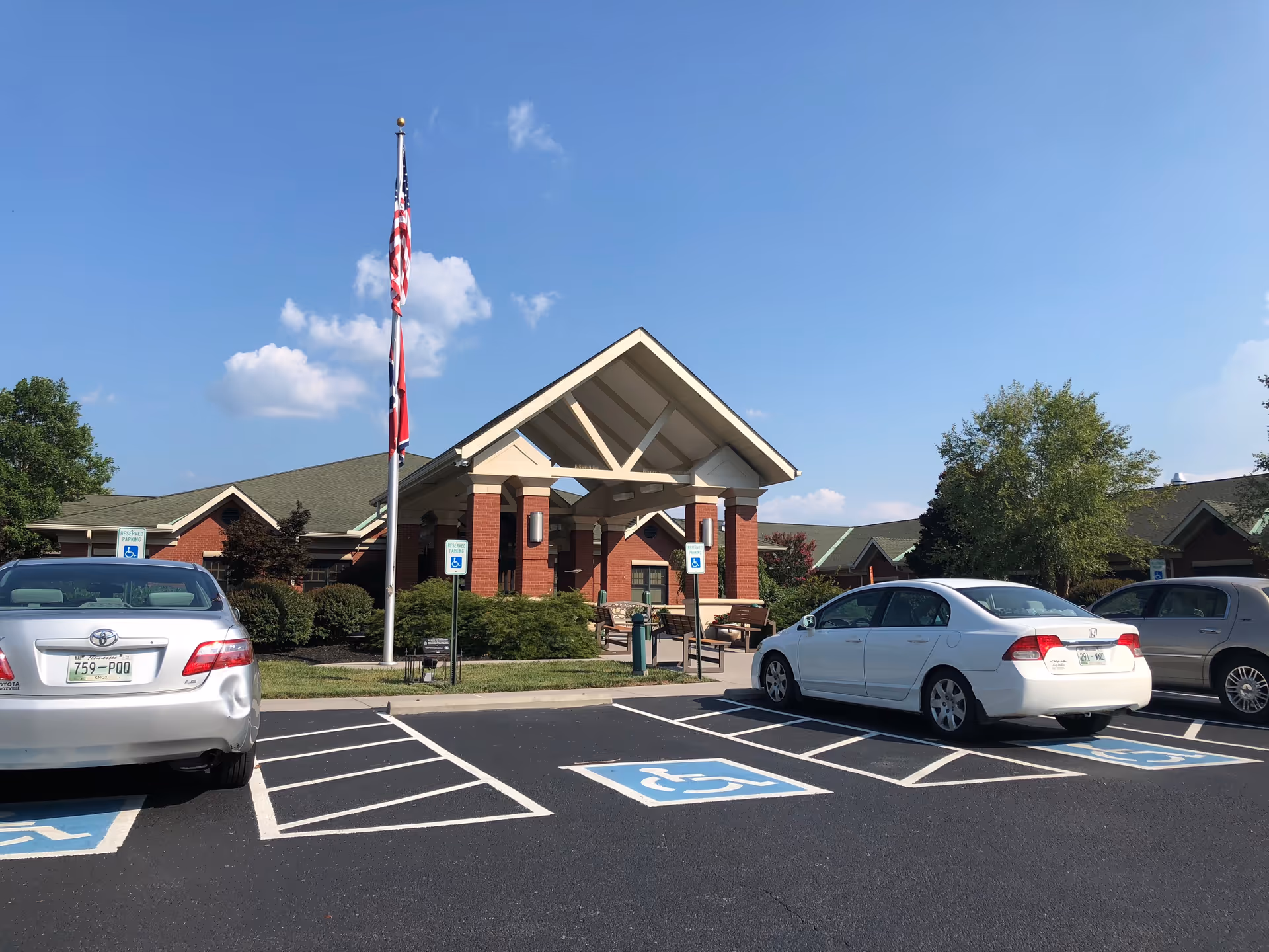 Exterior view of a brick senior living facility with flagpole and handicapped parking.