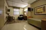 A small furnished bedroom in a senior facility with a bed, chair, and TV.
