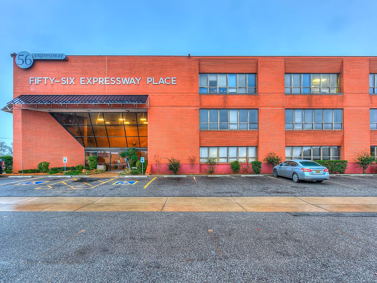Red brick building labeled Fifty-Six Expressway Place with glass entrance and parking.