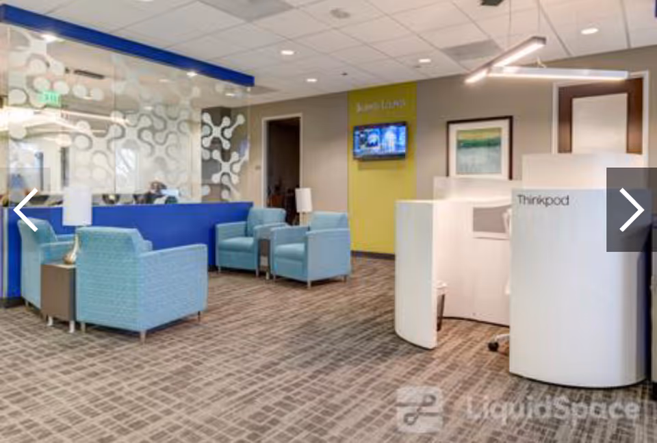 Modern facility lobby with blue seating, glass partition, and a curved white information kiosk.