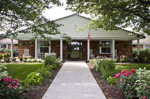 Front view of a single-story brick senior care facility with walkway and gardens.