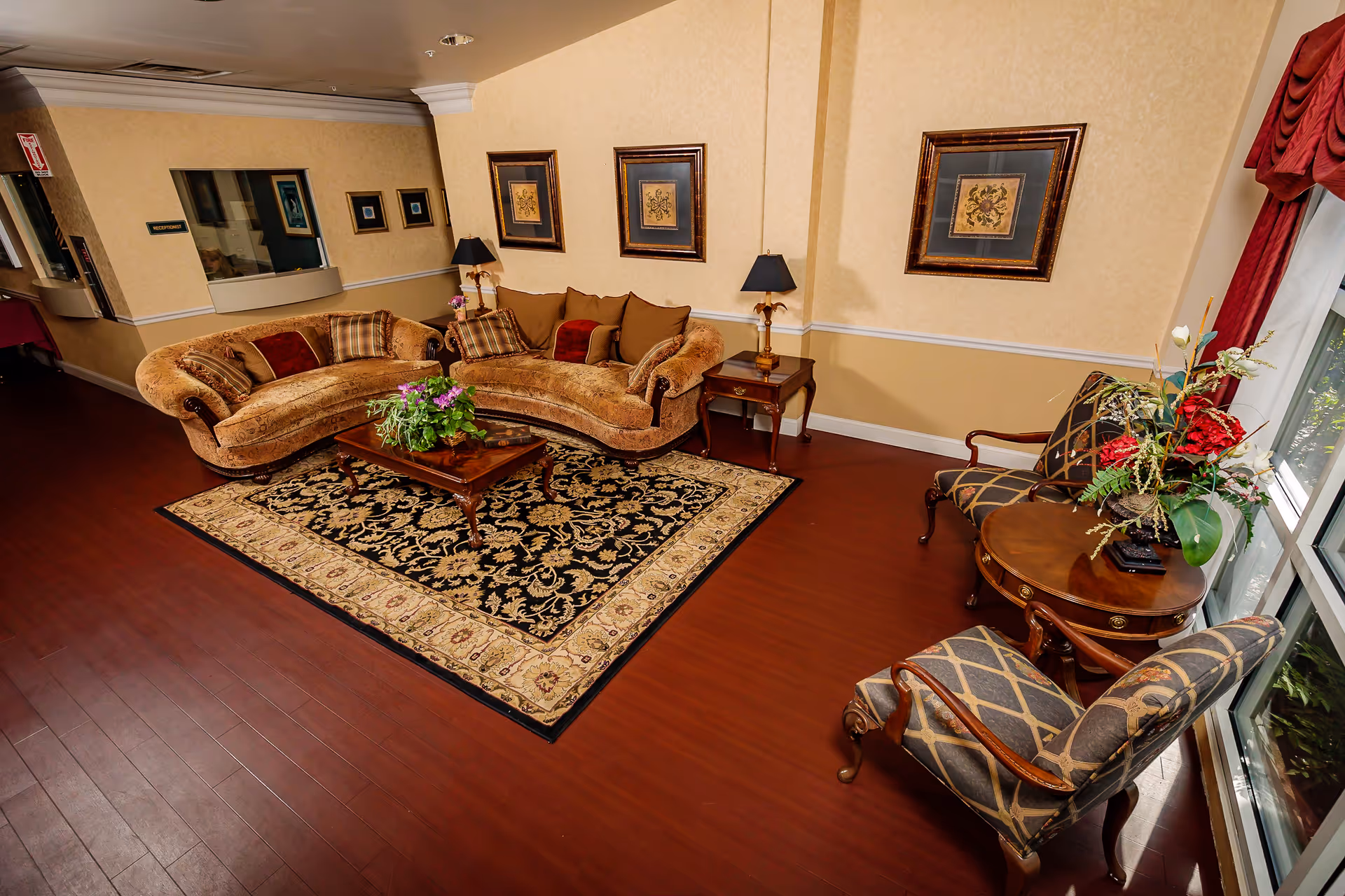 Decorative lounge area with curved sofas, a patterned rug, coffee table with flowers, accent chairs, and framed artwork on the walls.
