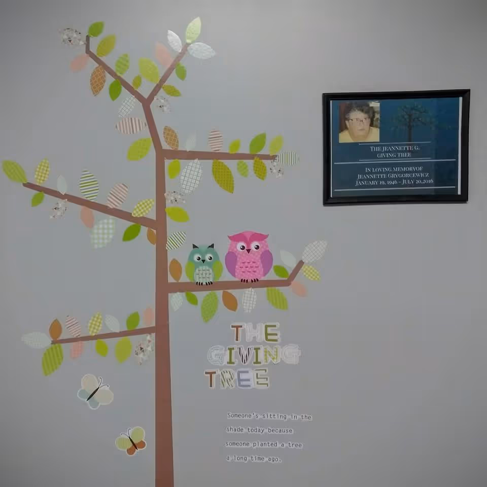 Wall mural of a tree with colorful leaves and two owls beside a plaque.