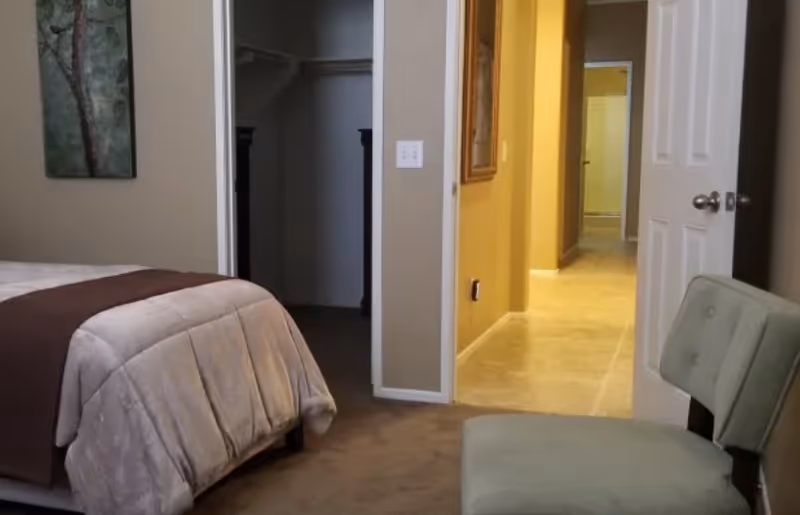 A bedroom with a bed, chair, and an open closet doorway leading to a hallway.